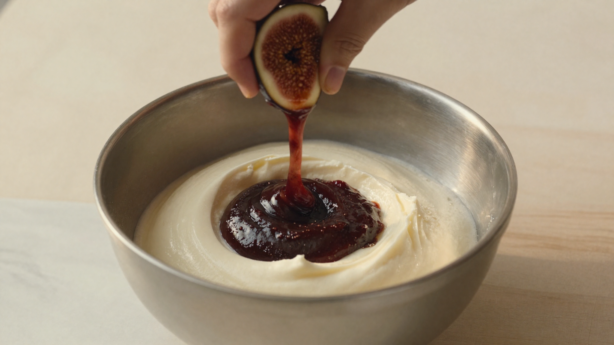 Dark fig puree being folded into a pale white gelato base in a stainless bowl