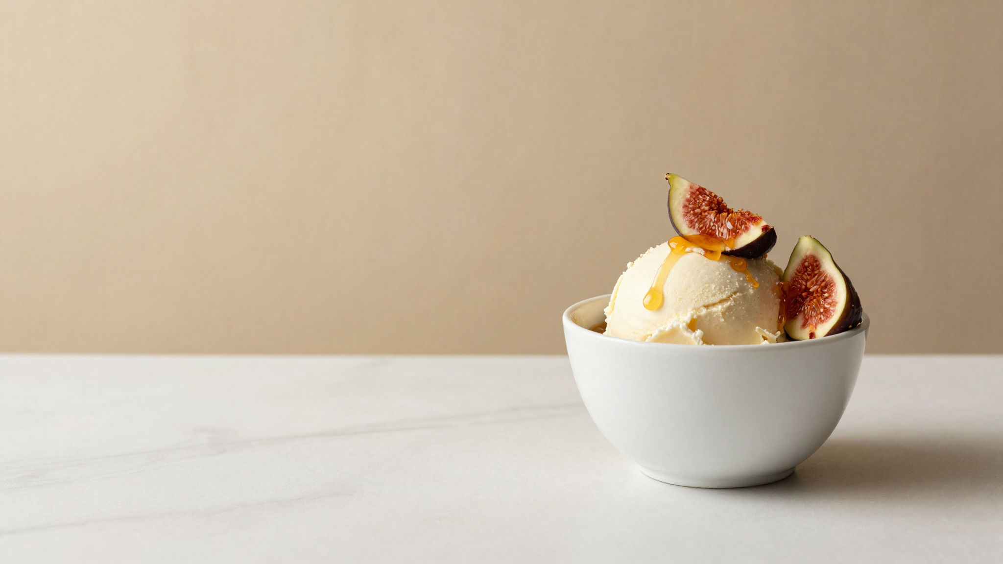A scoop of fig and honey gelato with fresh fig quarters and a honey drizzle in a white bowl