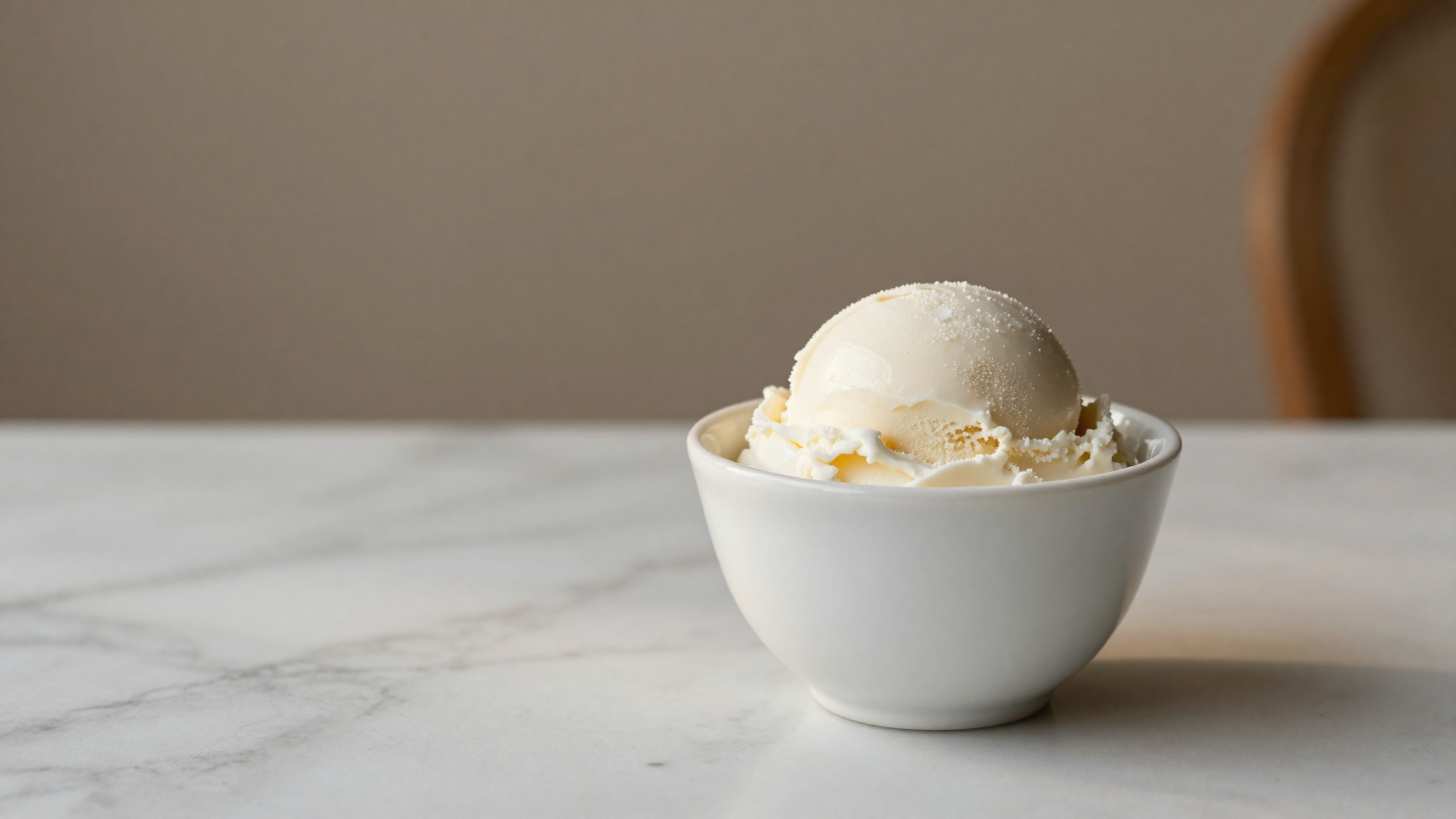 A small white ceramic cup of pure milk-white fior di latte gelato on marble