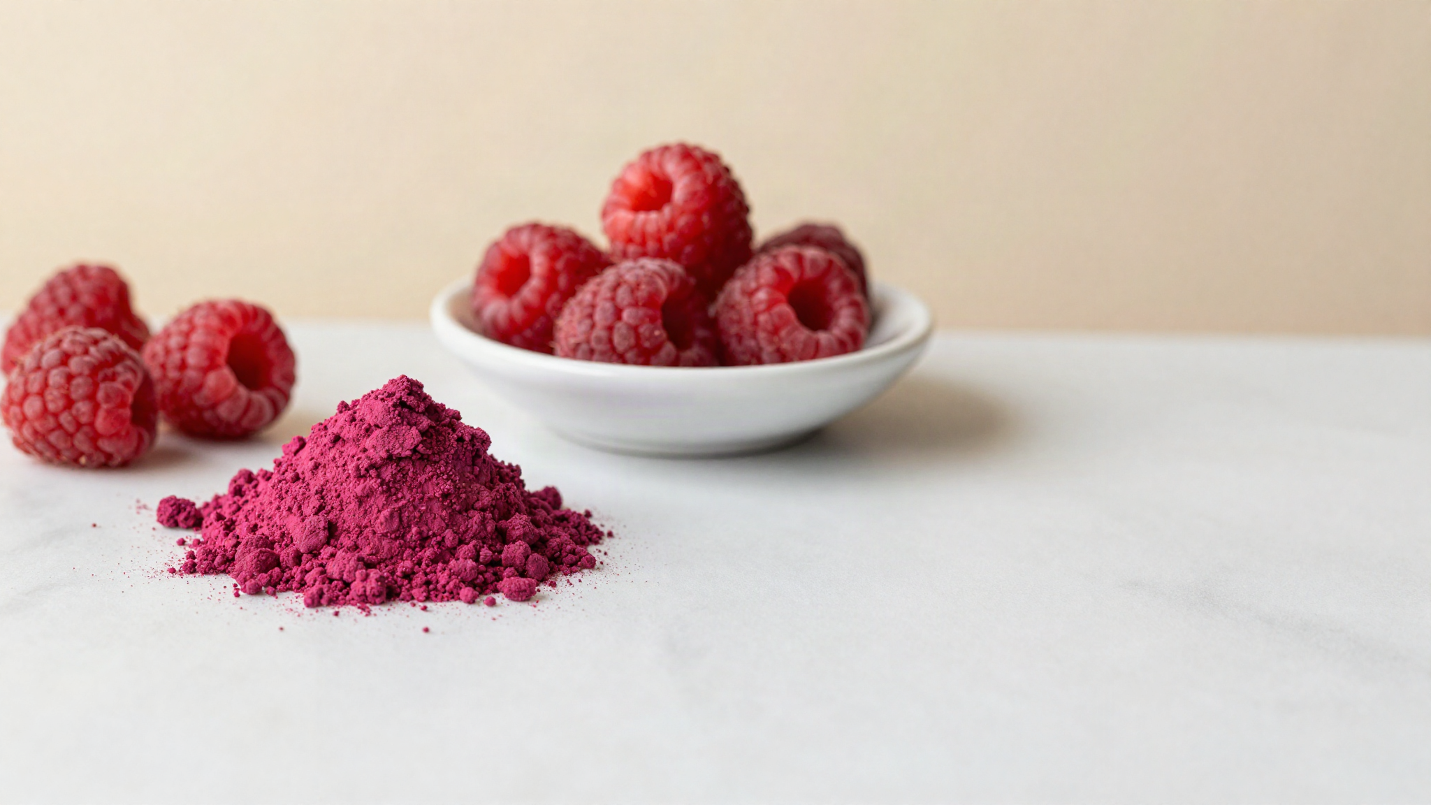 Freeze dried raspberry powder in a white ceramic dish with whole freeze dried raspberries on marble