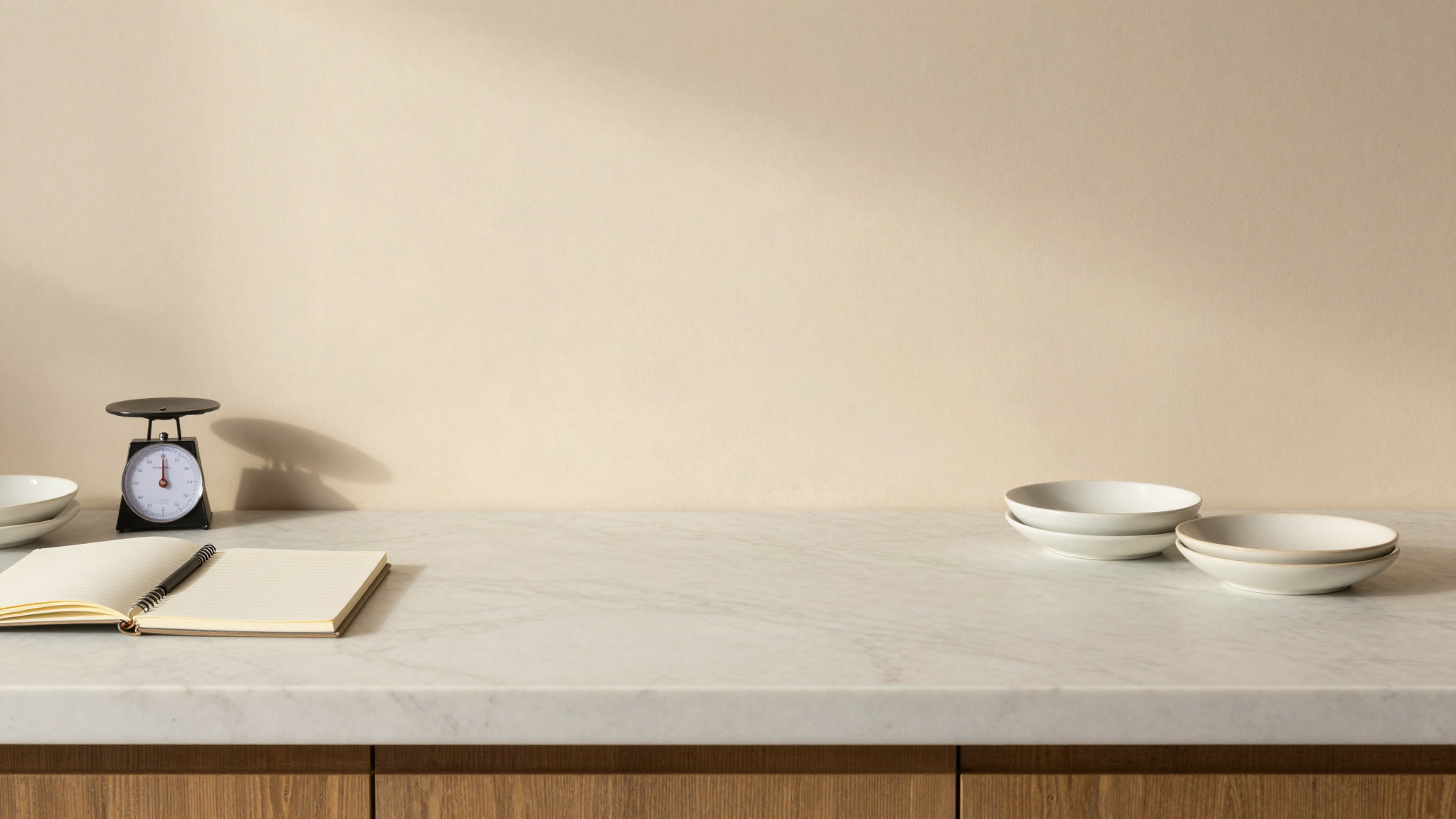 Marble lab counter seen from above with a notebook, a precision scale and ceramic dishes of gelato ingredients