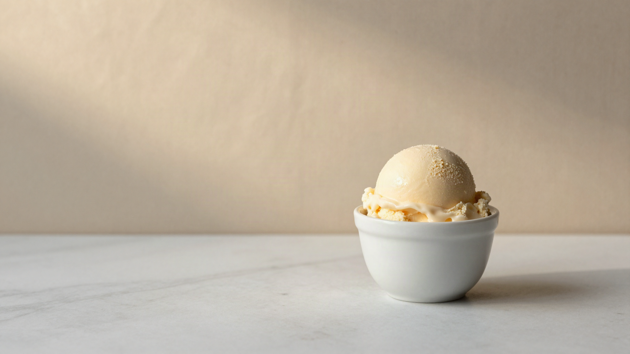 A freshly drawn scoop of pale italian gelato in a small white ceramic cup on a marble counter