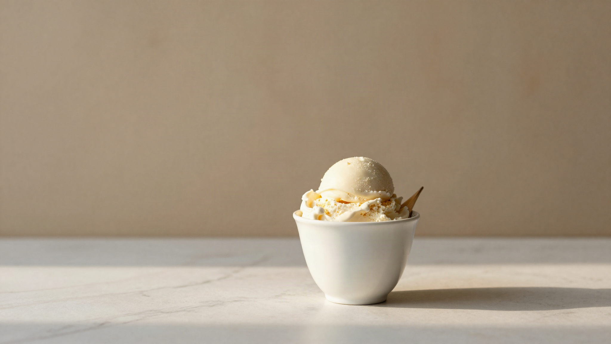 Two small ceramic cups of white fior di latte gelato with clean quenelles on a marble counter