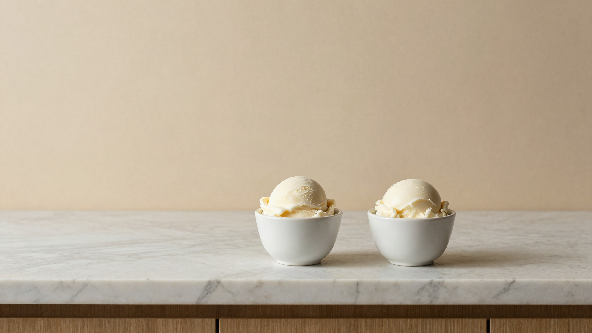 Two ceramic cups of white fior di latte gelato with clean quenelles on a marble counter