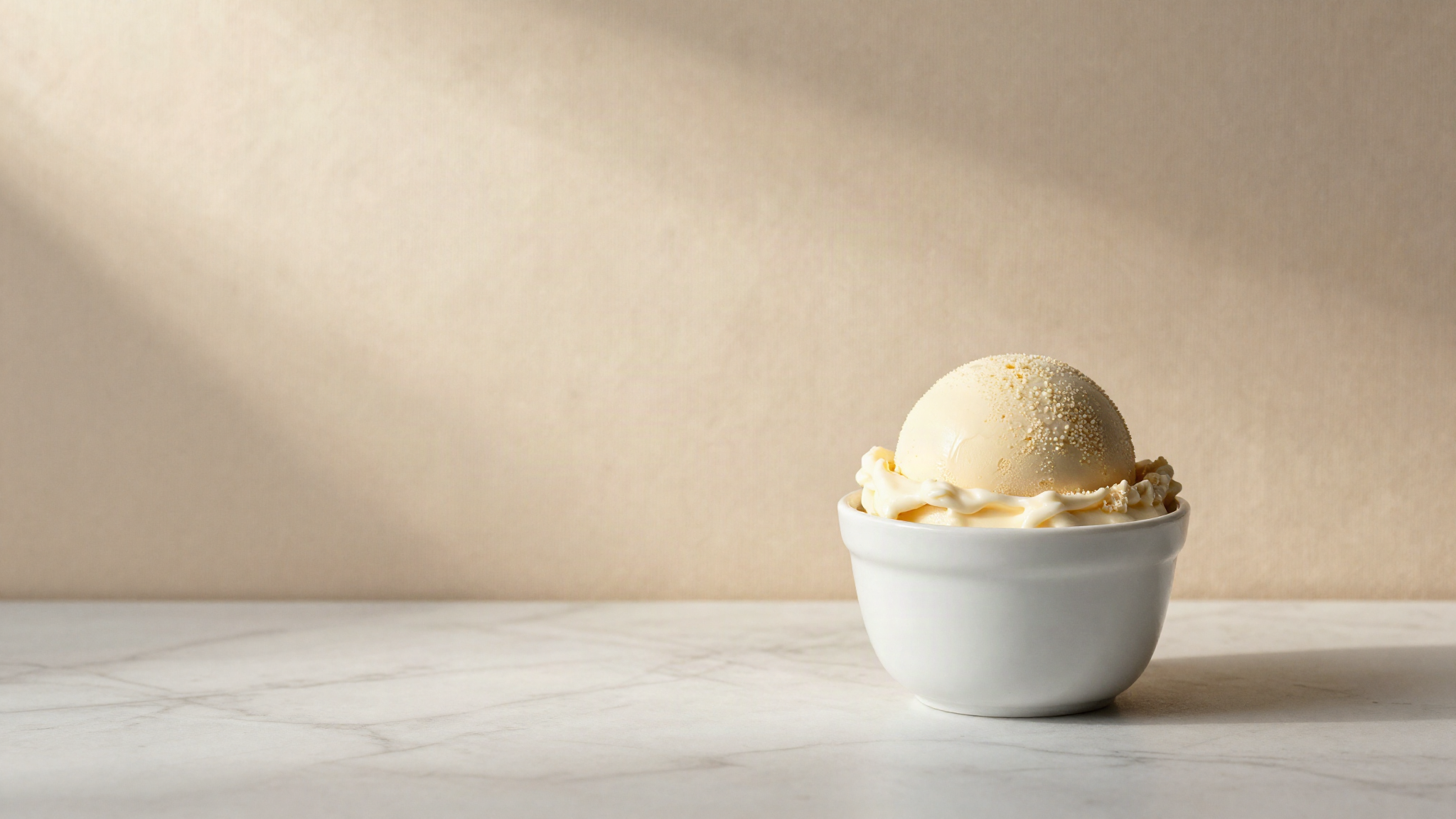 Pale scoop of italian gelato in a small white ceramic cup on a marble counter