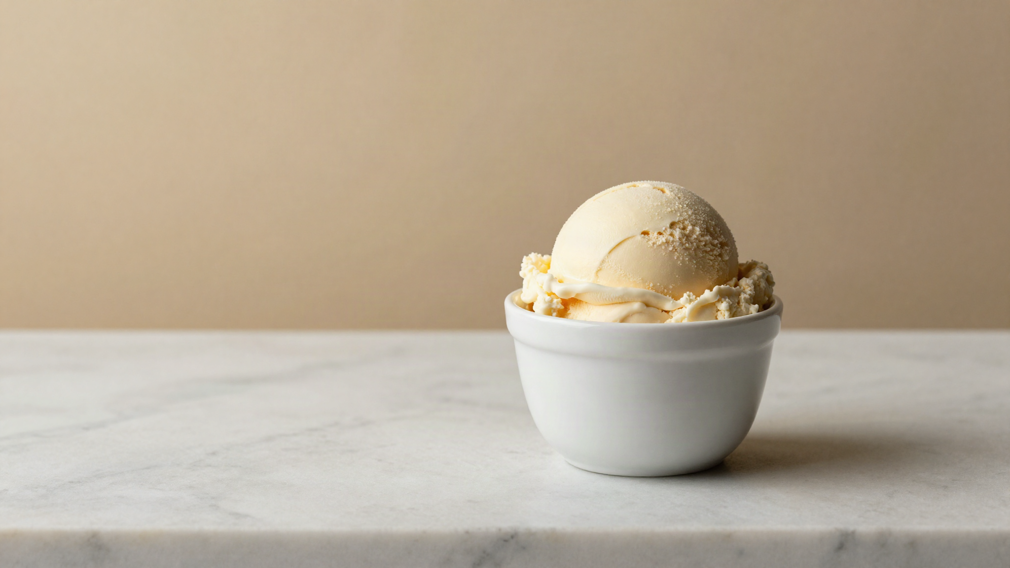 A single clean scoop of pale fiordilatte gelato in a small white ceramic cup on white marble