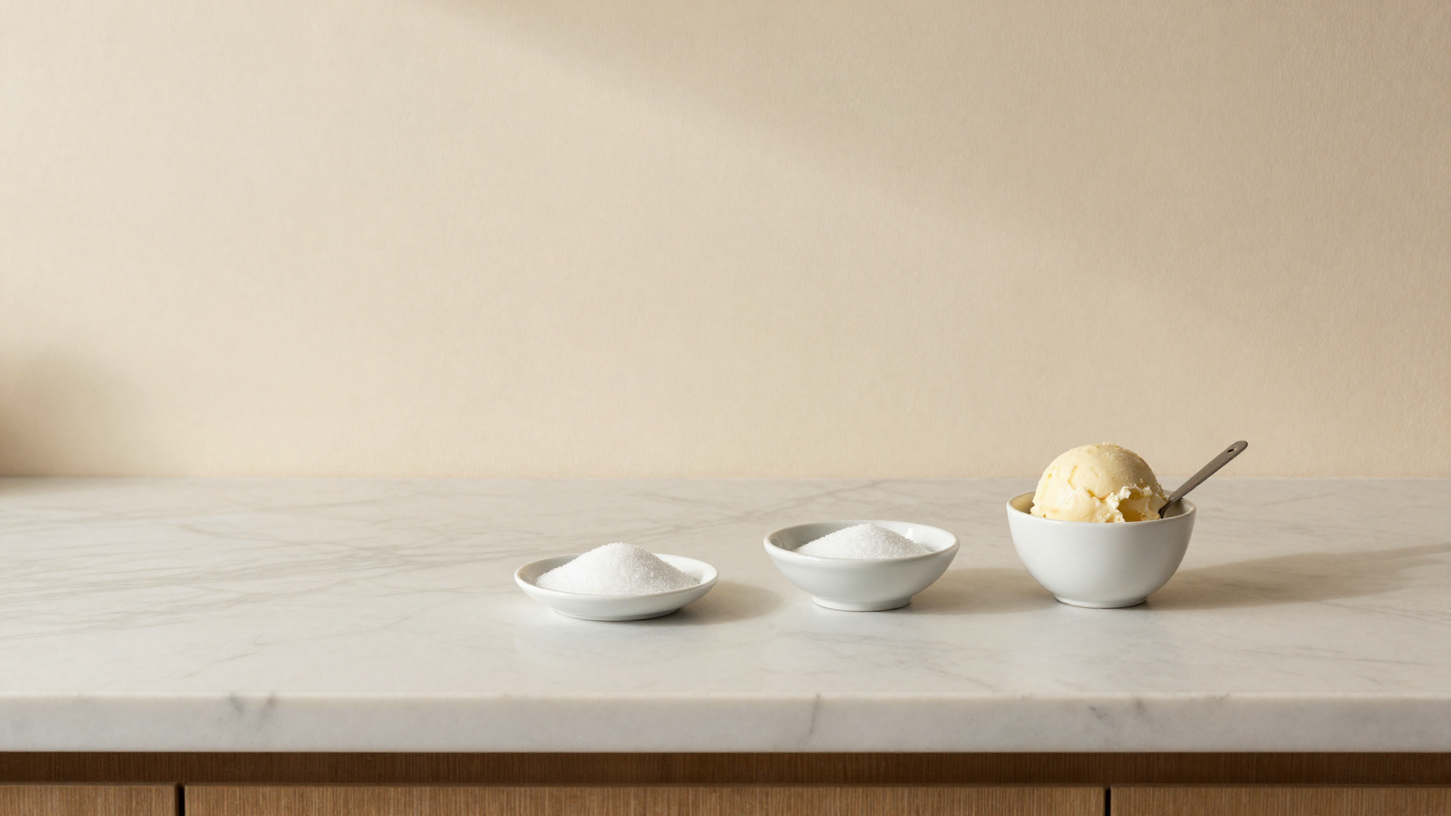 A marble counter with small dishes of sugar, a tiny scale and a scoop of gelato in a white ceramic cup