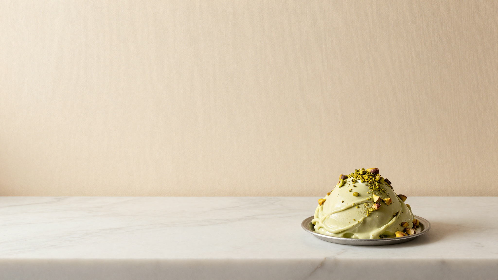 A single pozzetto well of dense pistachio italian gelato seen from above on a warm marble surface