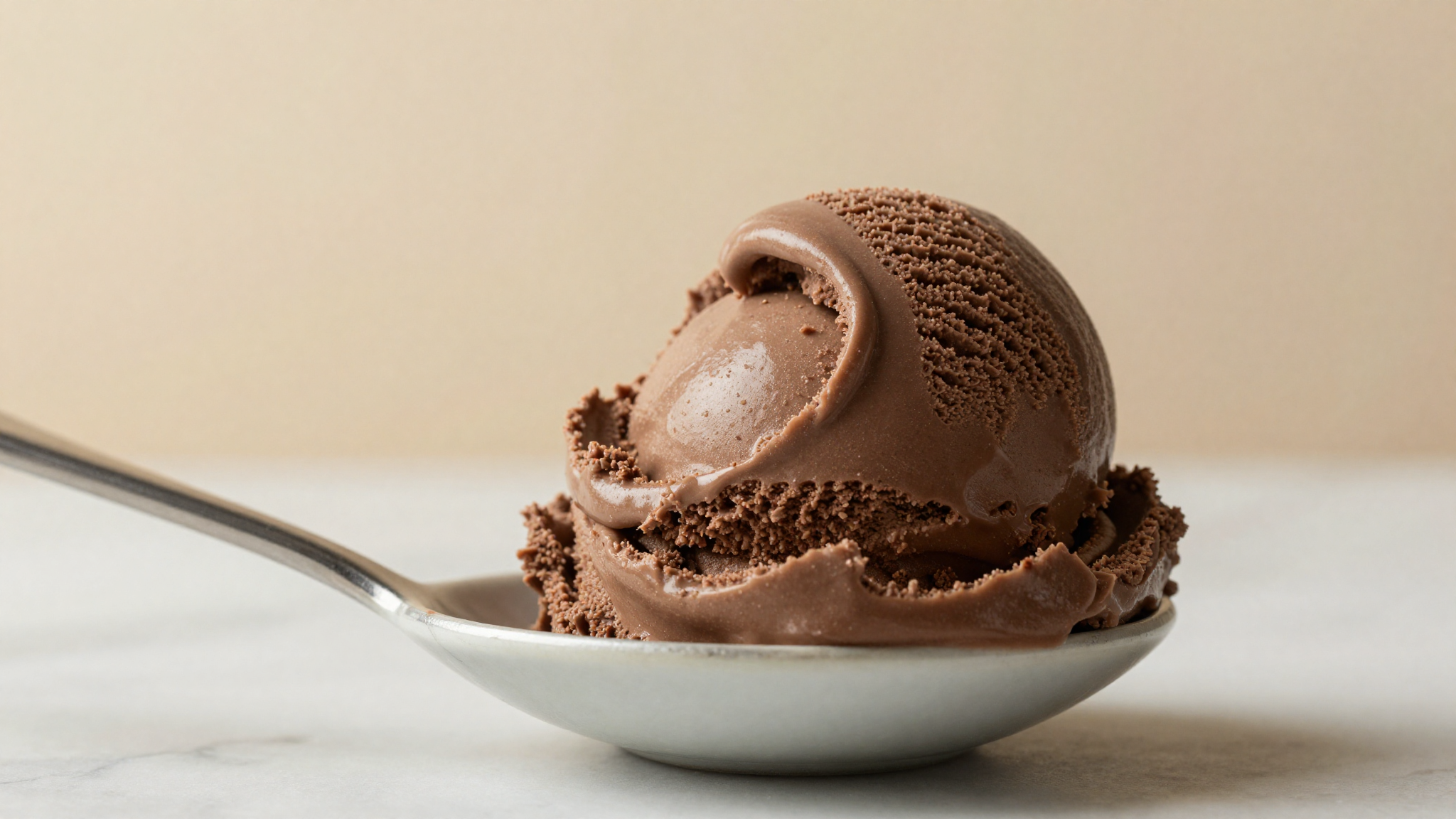 Macro close-up of a single perfect curl of dense italian chocolate gelato lifted onto a small ceramic spoon