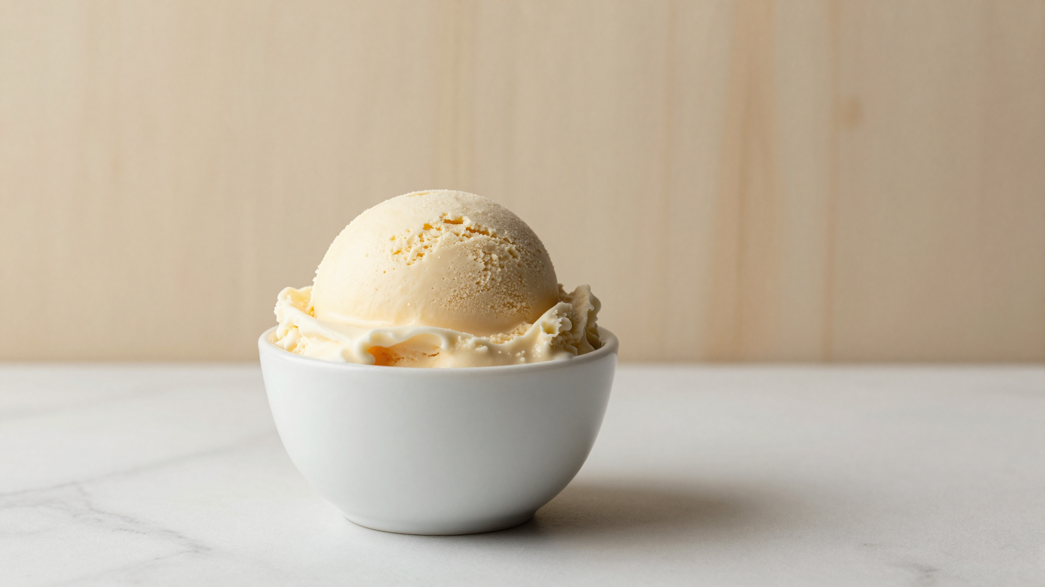 A creamy pale gelato scoop and a glossy ruby Italian water ice side by side in white cups on marble