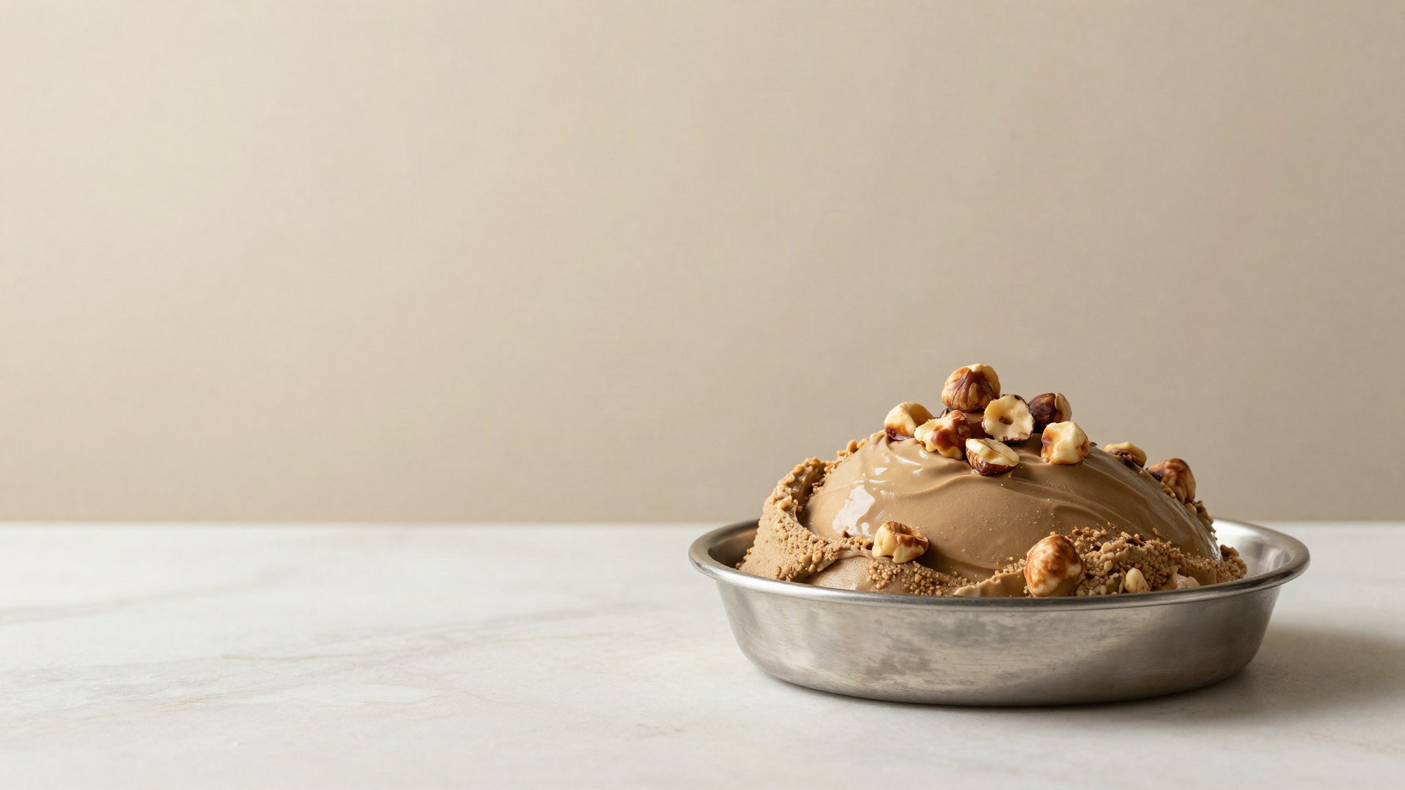 Stainless gelato pan of glossy light brown gianduja gelato topped with whole toasted hazelnuts