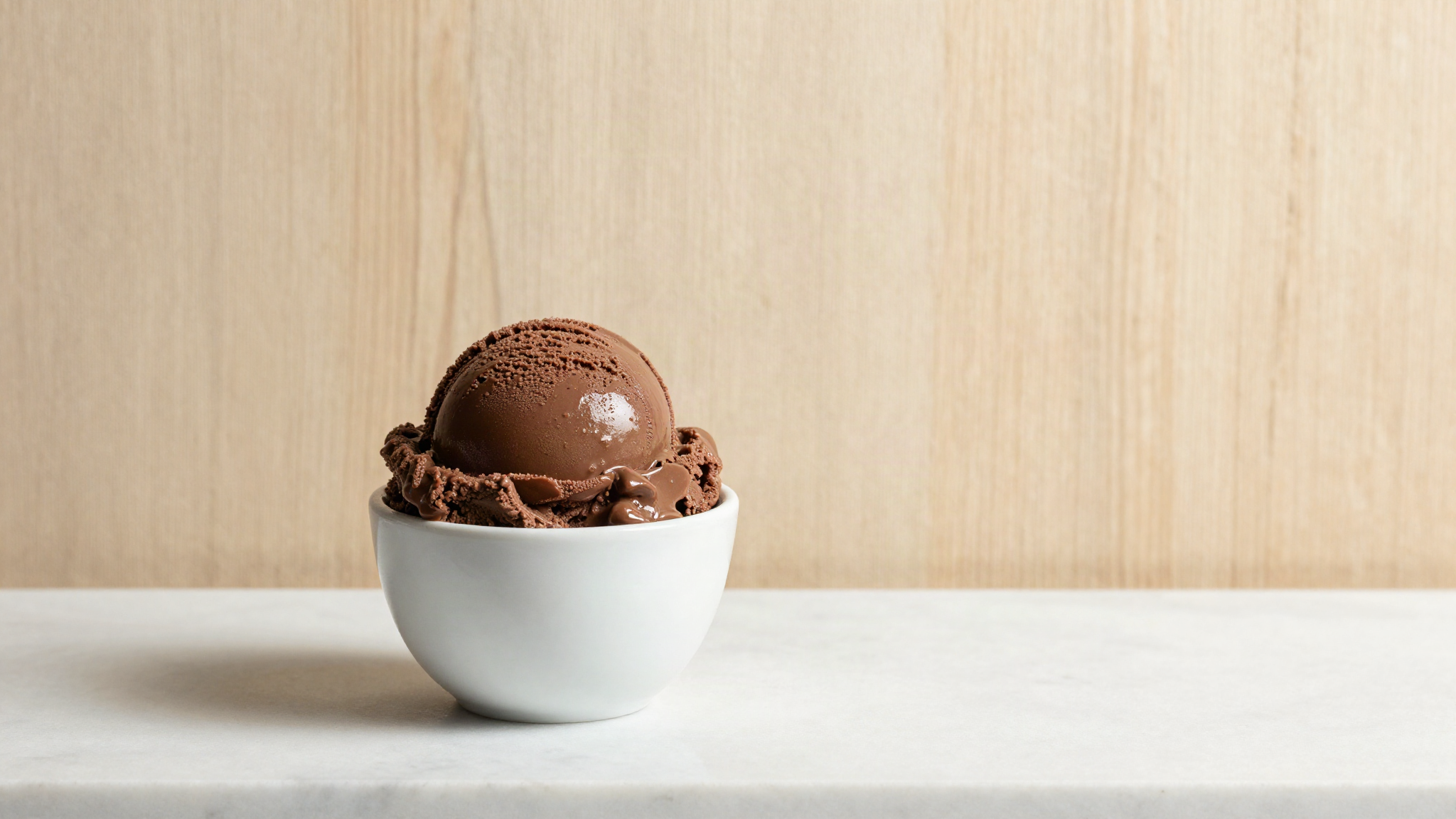 A soft glossy scoop of dark chocolate gelato in a white ceramic cup