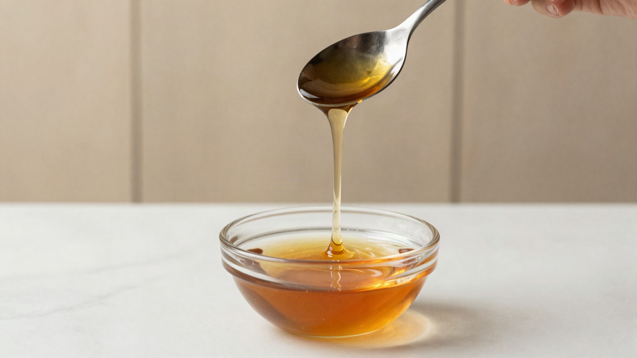 Thick amber glucose syrup falling in a slow ribbon from a spoon into a glass bowl