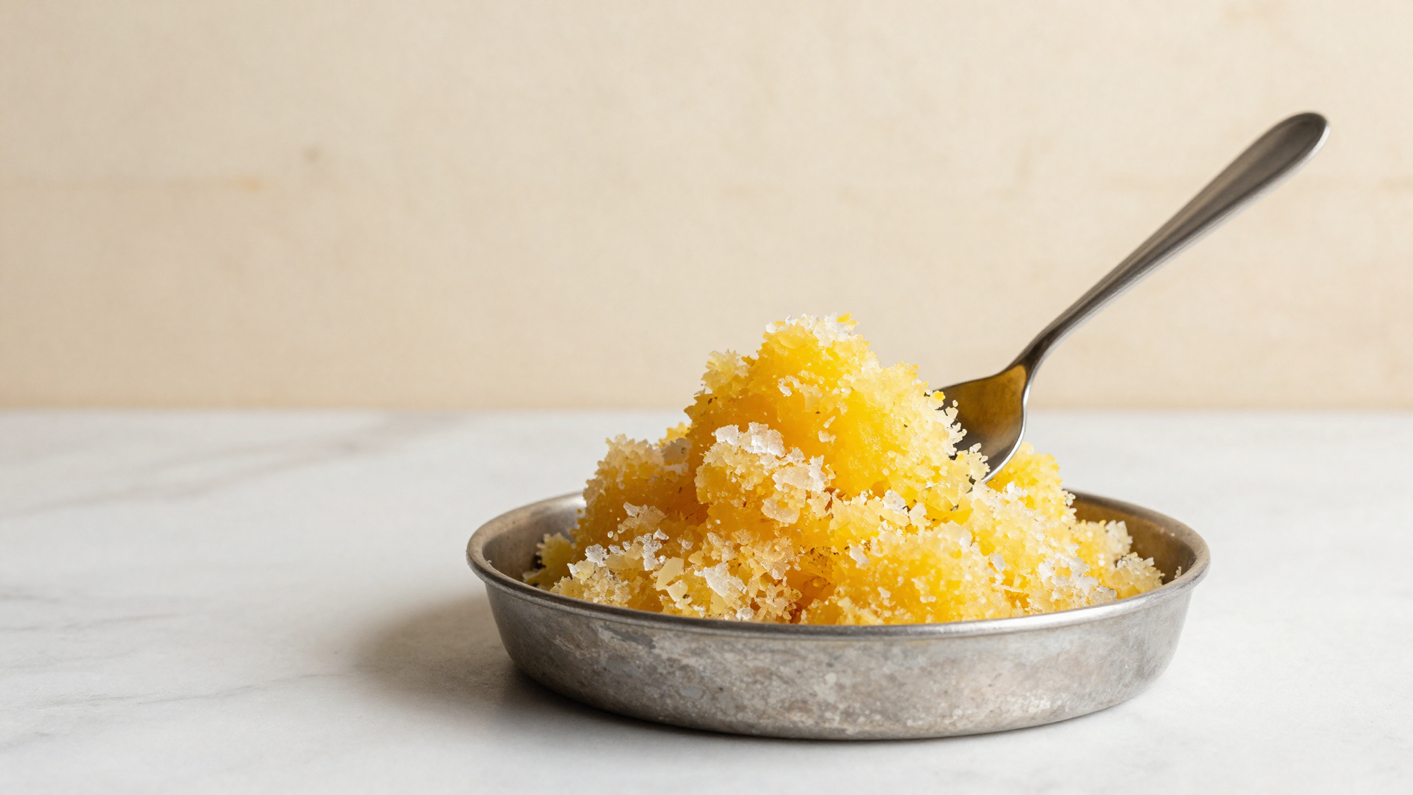 Bright citrus granita being raked with a fork in a metal tray