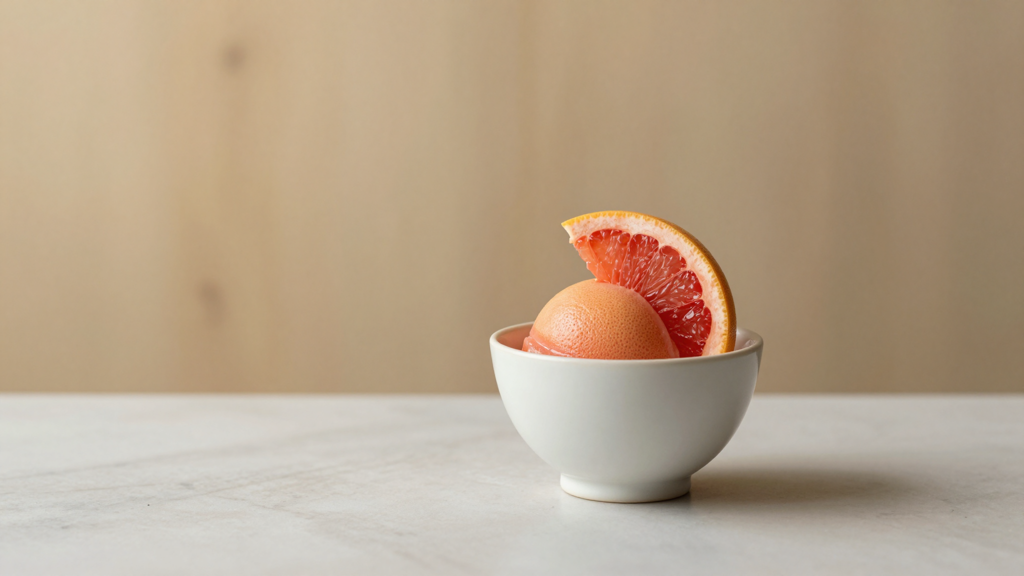 A serving of pale pink grapefruit sorbet in a ceramic cup with a single citrus segment