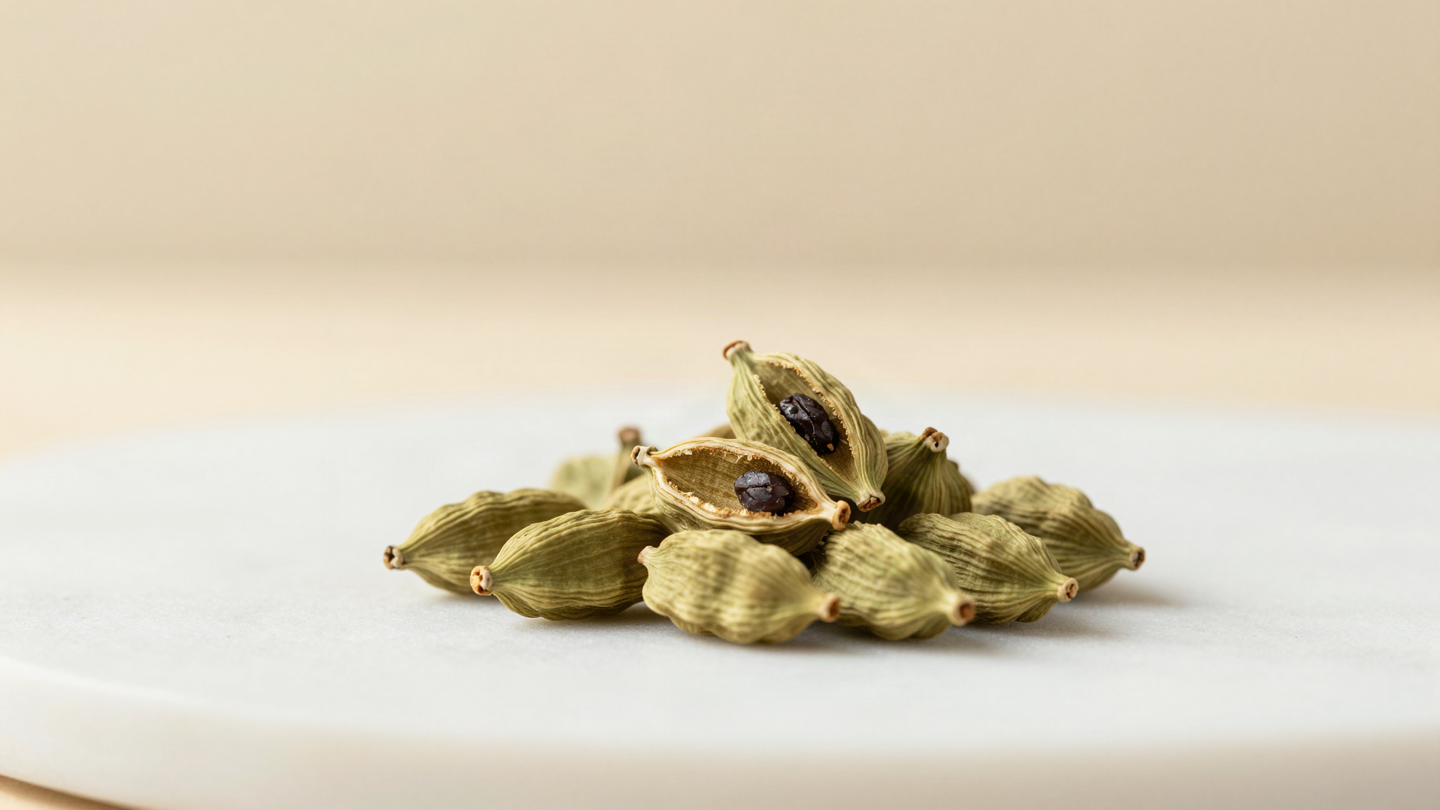 A small pile of pale green cardamom pods with two pods split open showing the dark seeds inside