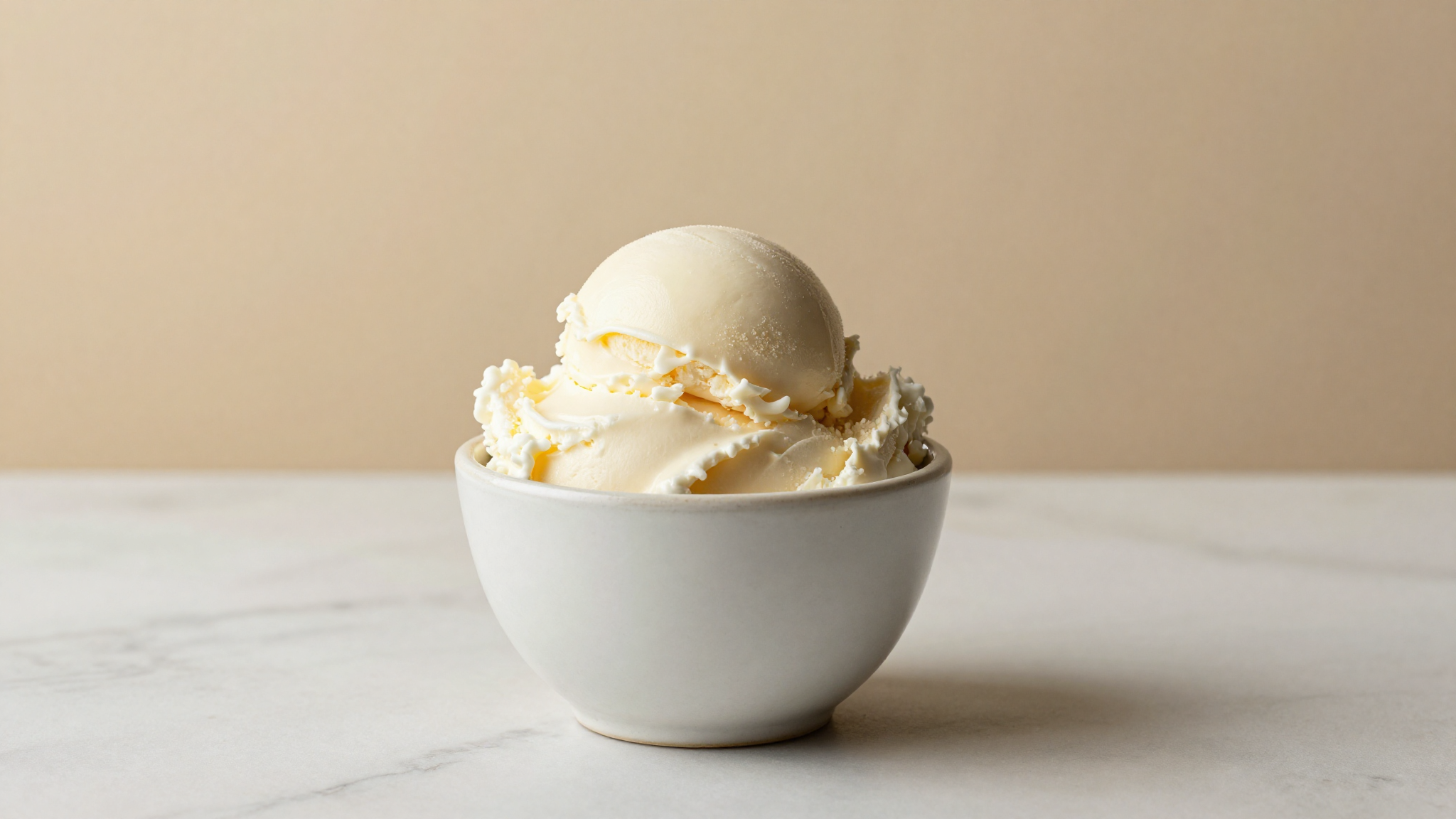 A smooth dense scoop of gelato in a ceramic cup on marble, showing the fine texture a stabiliser protects
