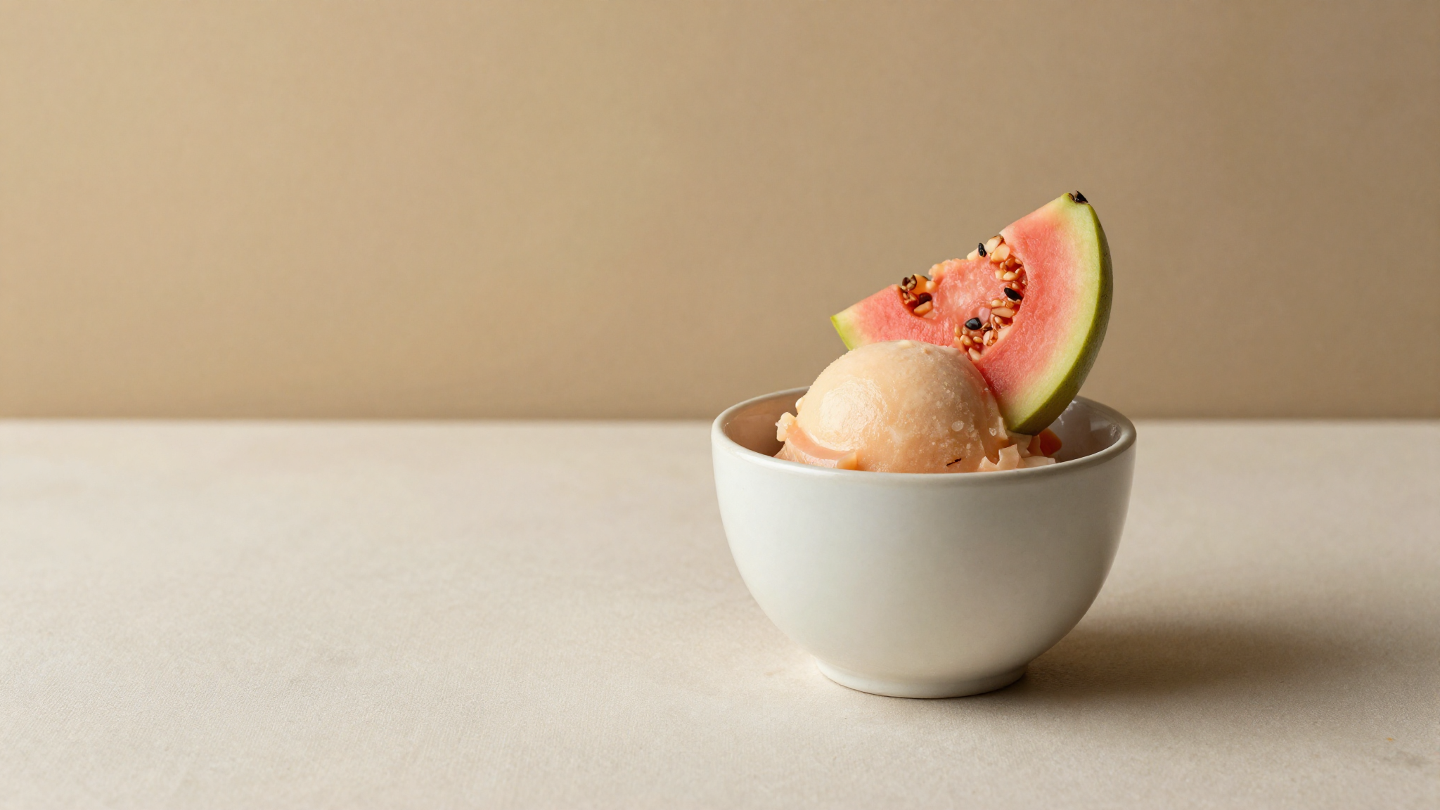 A white ceramic bowl of pale guava sorbetto garnished with a slice of fresh pink guava