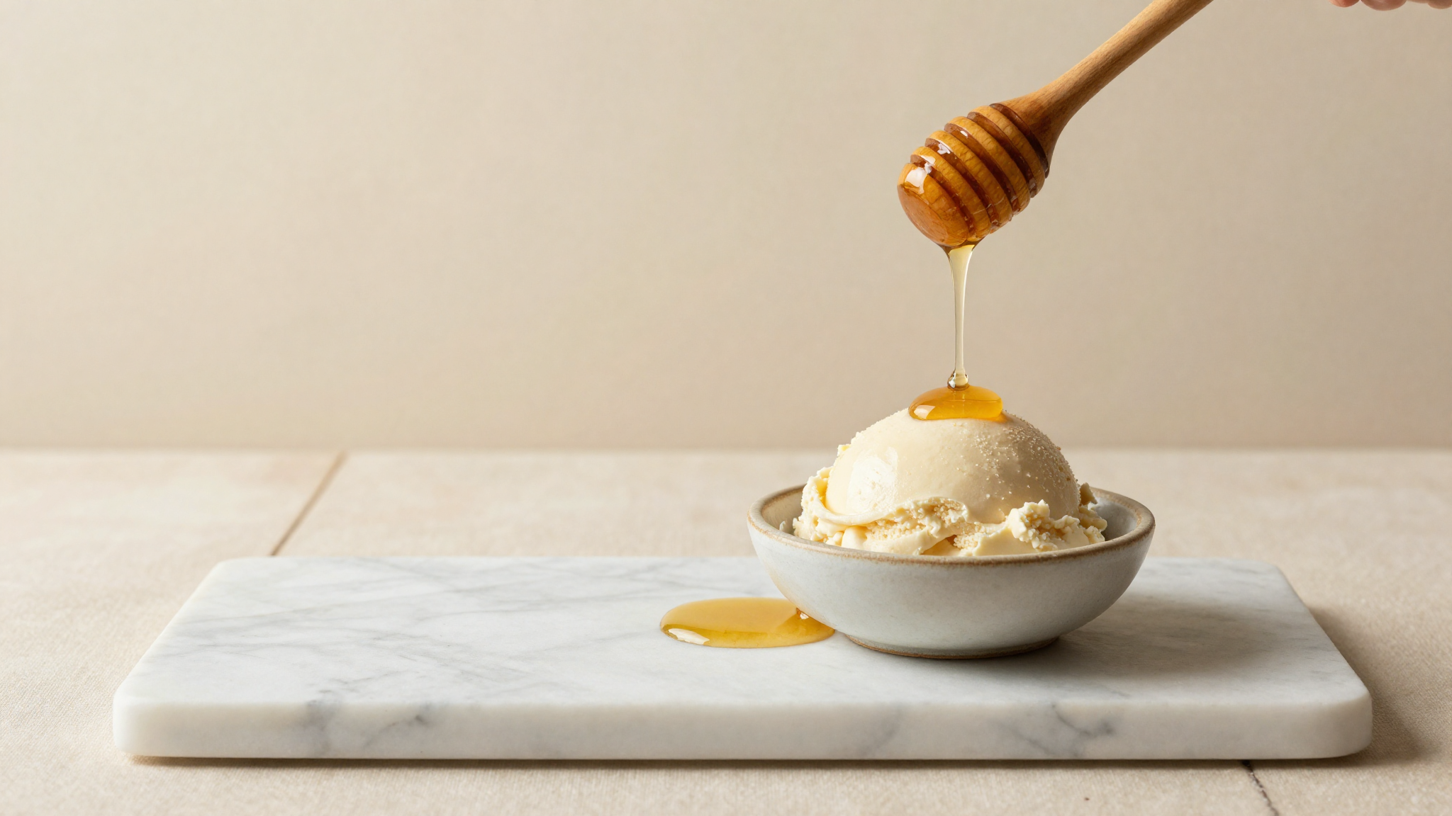 Jar of raw honey drizzling onto a marble slab beside a small dish of gelato mix