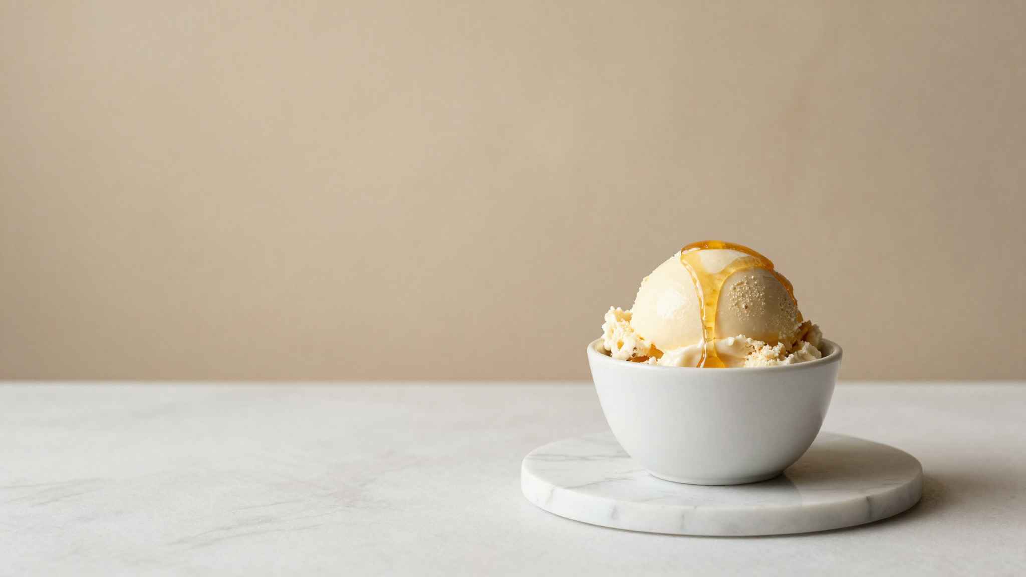 A scoop of pale honey gelato drizzled with honey in a white ceramic cup