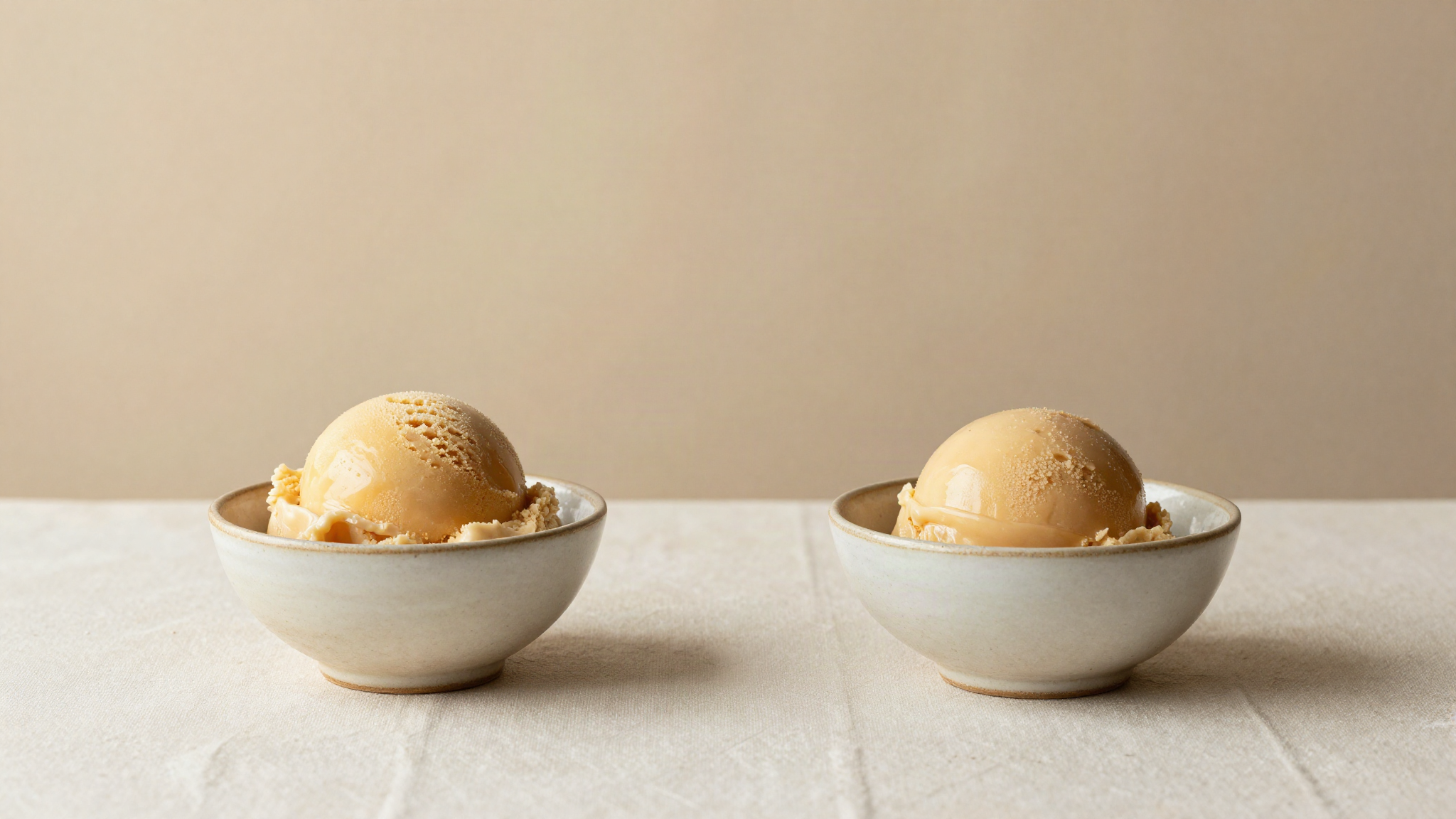 Two identical small ceramic bowls of gelato side by side on light cream linen, one slightly darker than the other