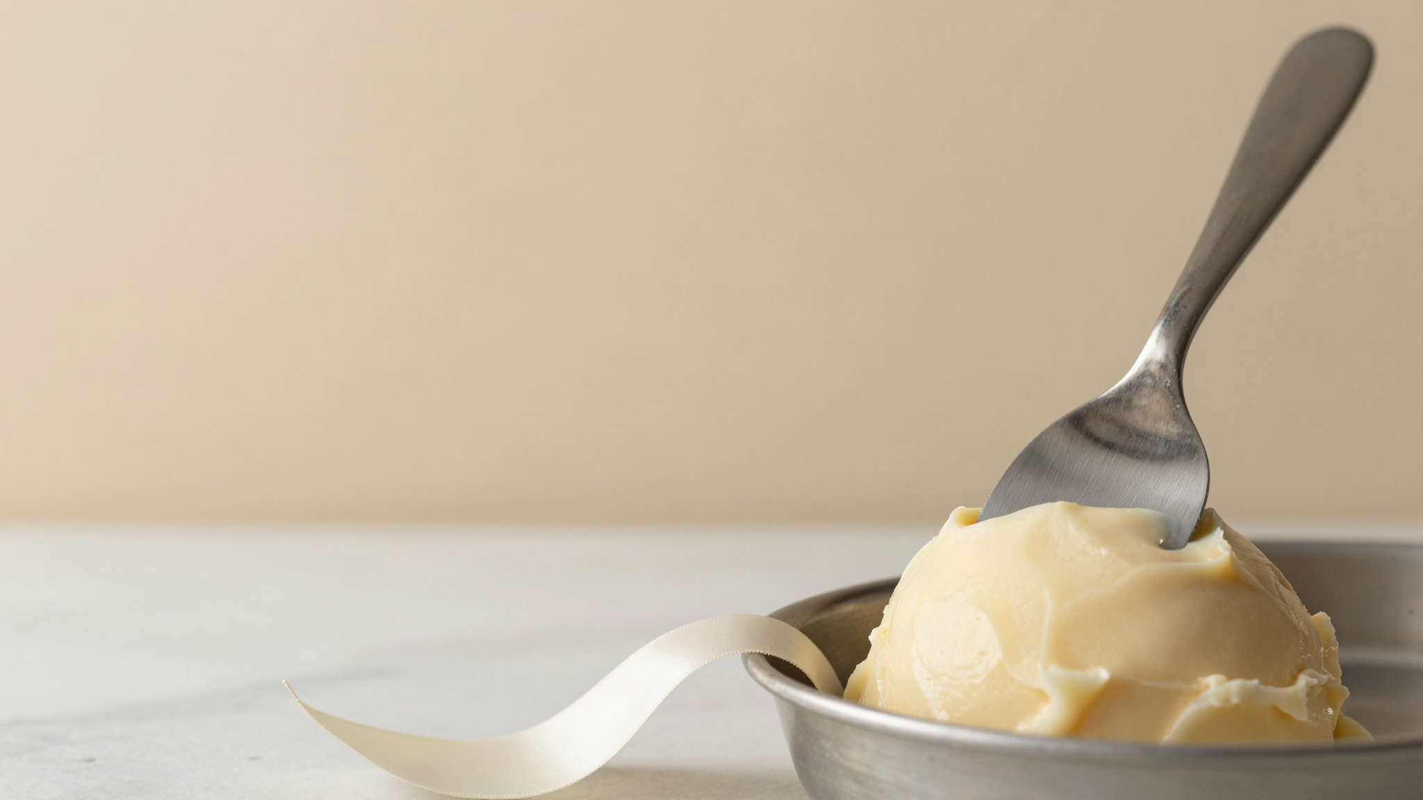 A stainless steel spatula resting against a smooth glossy ribbon of freshly extruded gelato in a metal pan