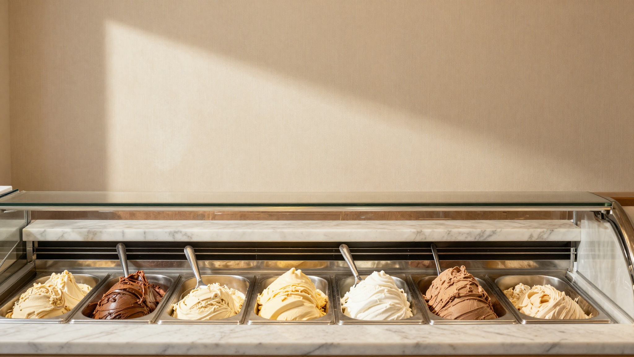 An elegant italian gelateria counter with several pozzetti showcasing different gelato flavors viewed from above on brass and marble surfaces