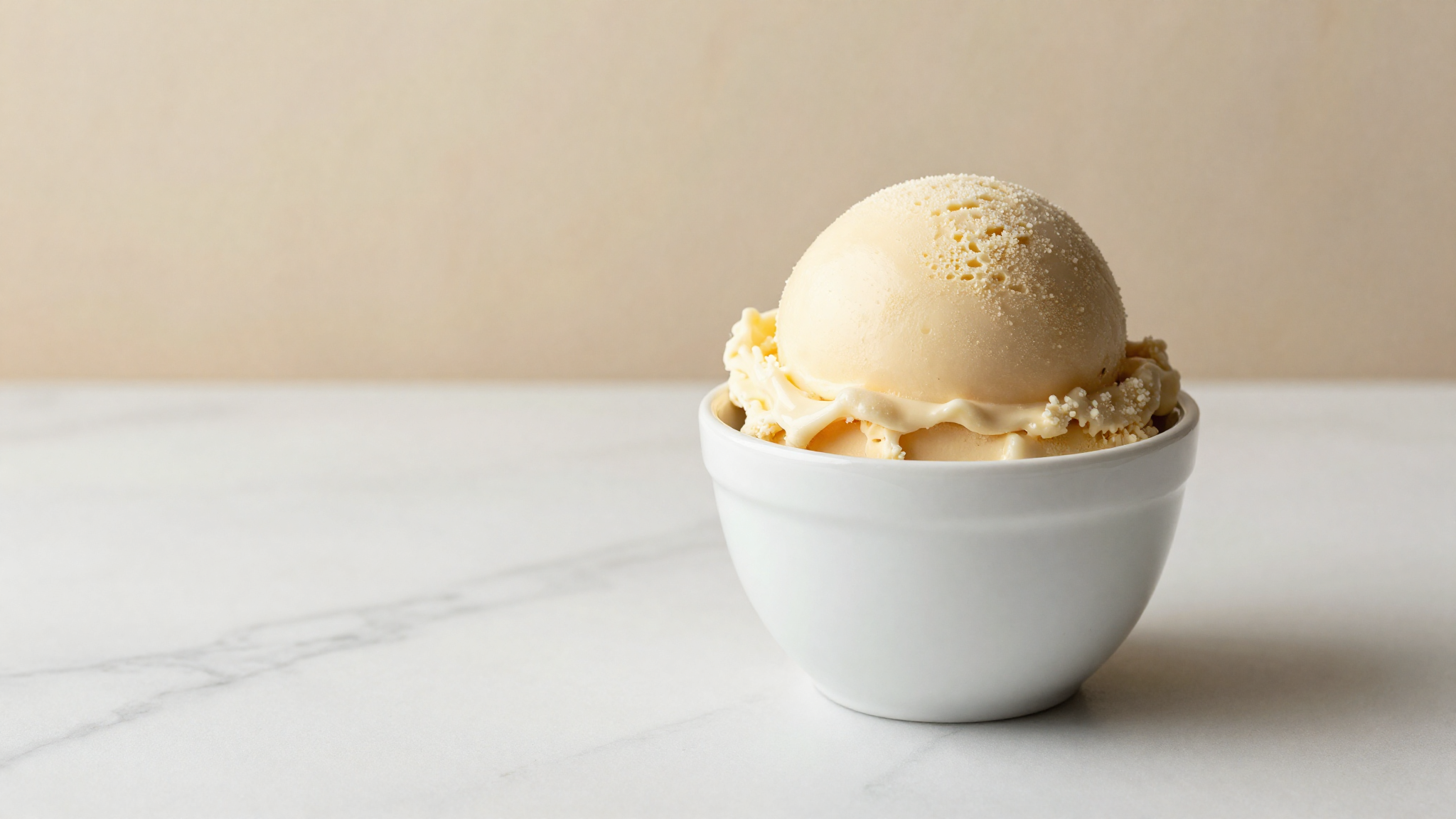 A freshly drawn scoop of italian gelato with a glossy ultra-smooth surface in a white ceramic cup on marble