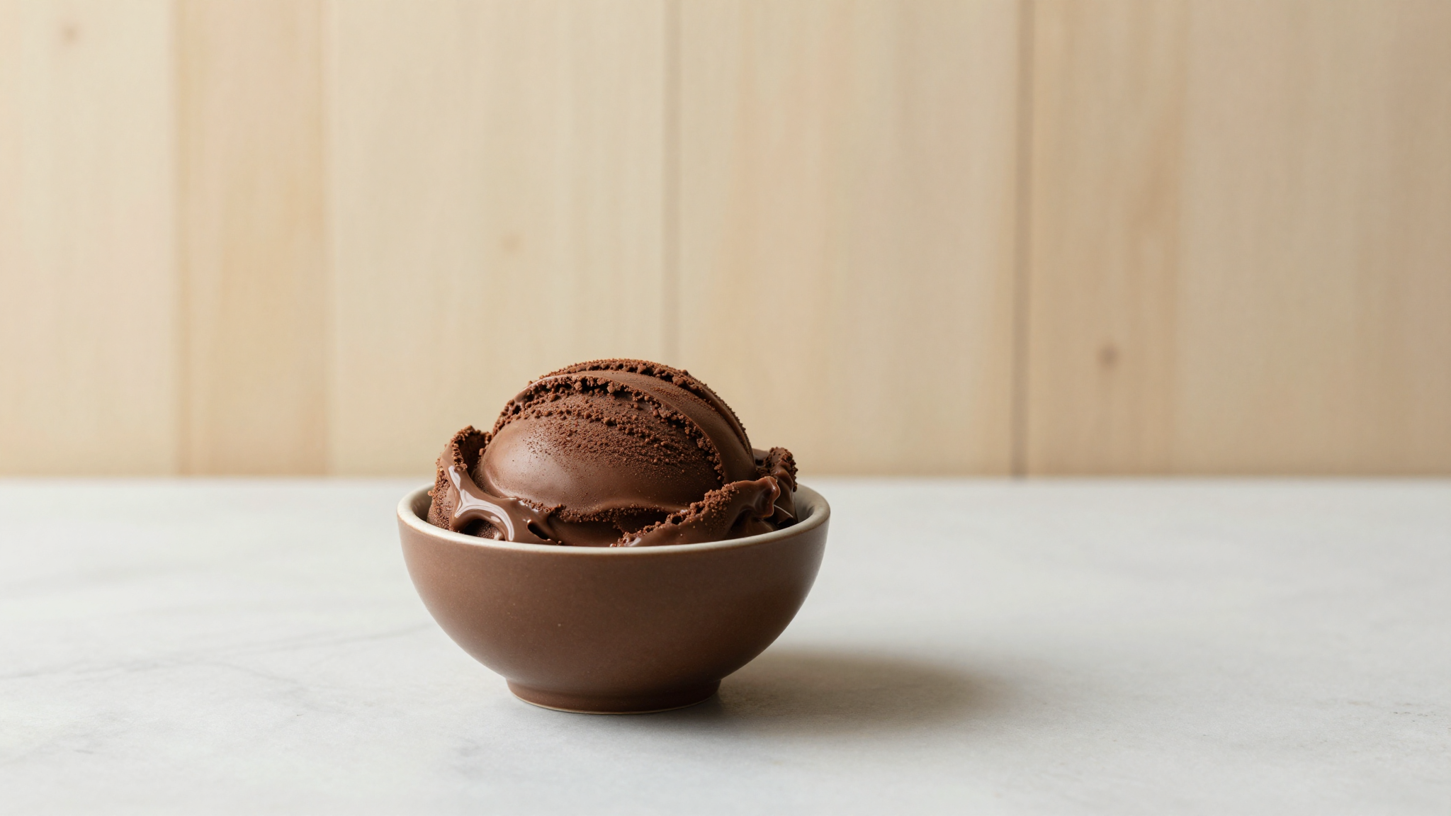 A small bowl of dark chocolate gelato glistening with cocoa butter sheen on a marble counter