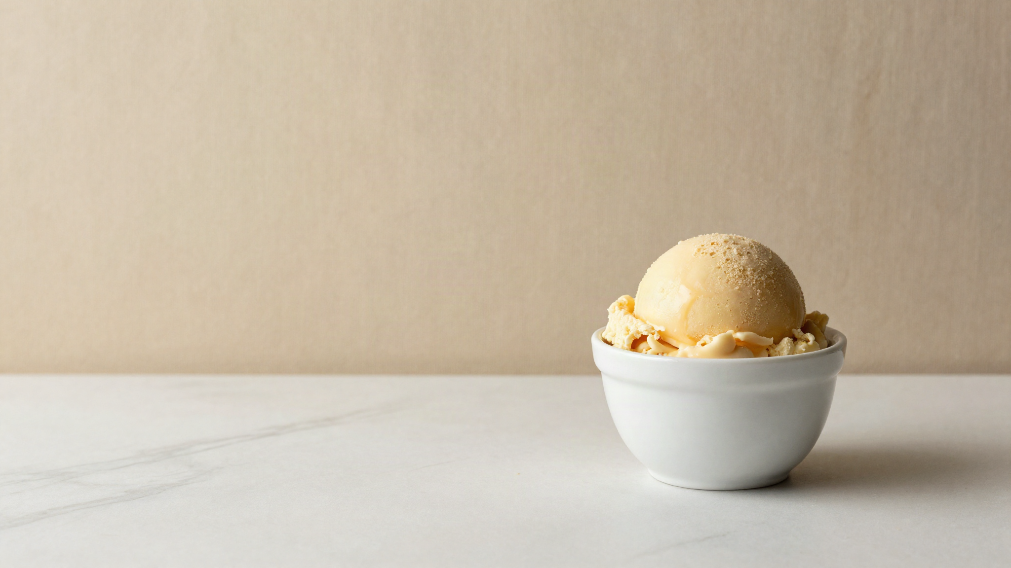 A freshly drawn scoop of pale golden honey gelato in a small white ceramic cup on marble