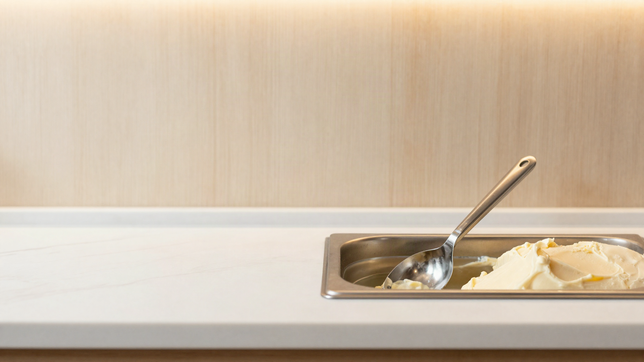 A stainless steel gelato spade resting in a small water filled dipper well beside an open pan of pale gelato in a clean italian display counter