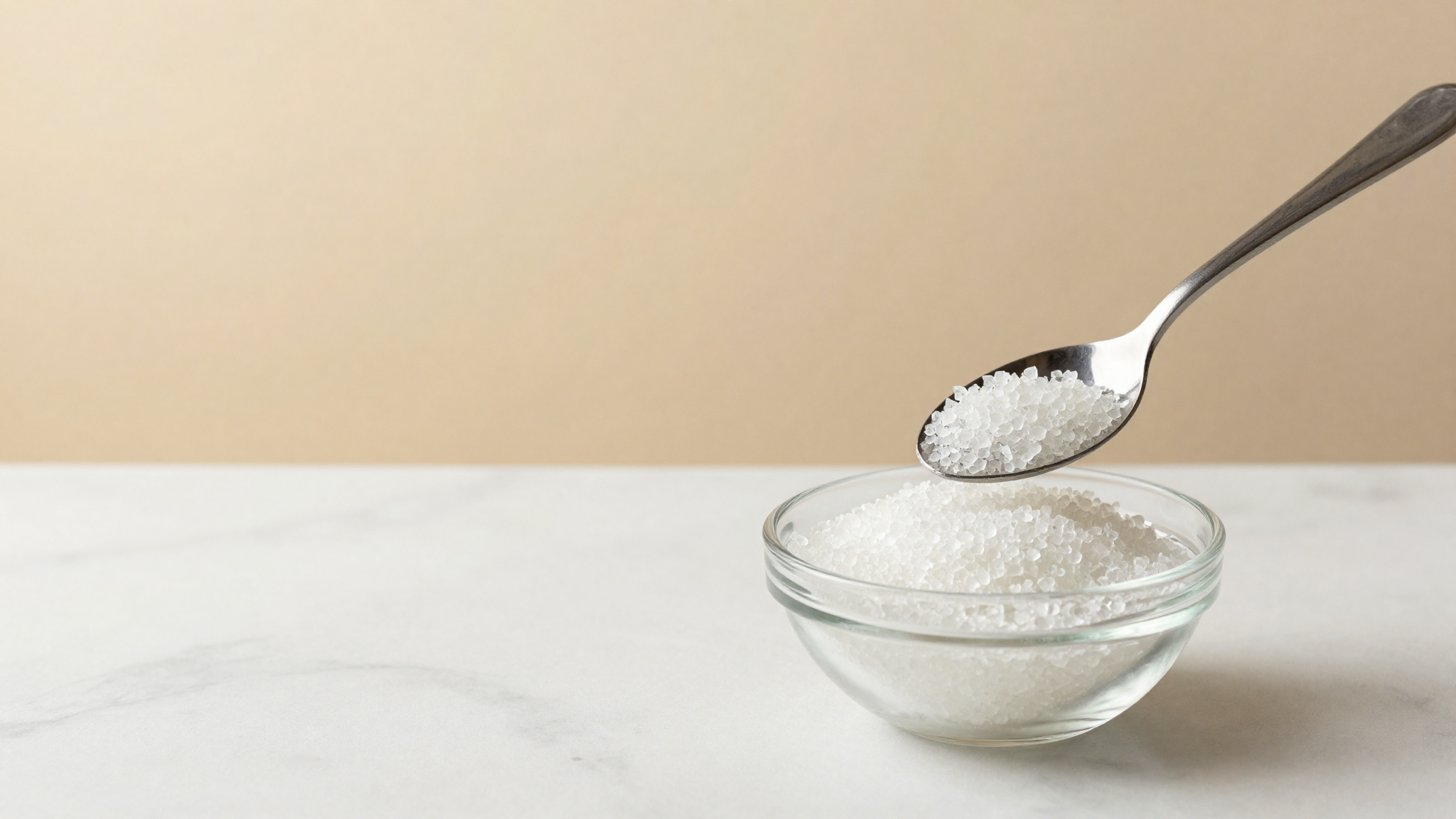A spoonful of translucent isomalt crystals held over a glass bowl