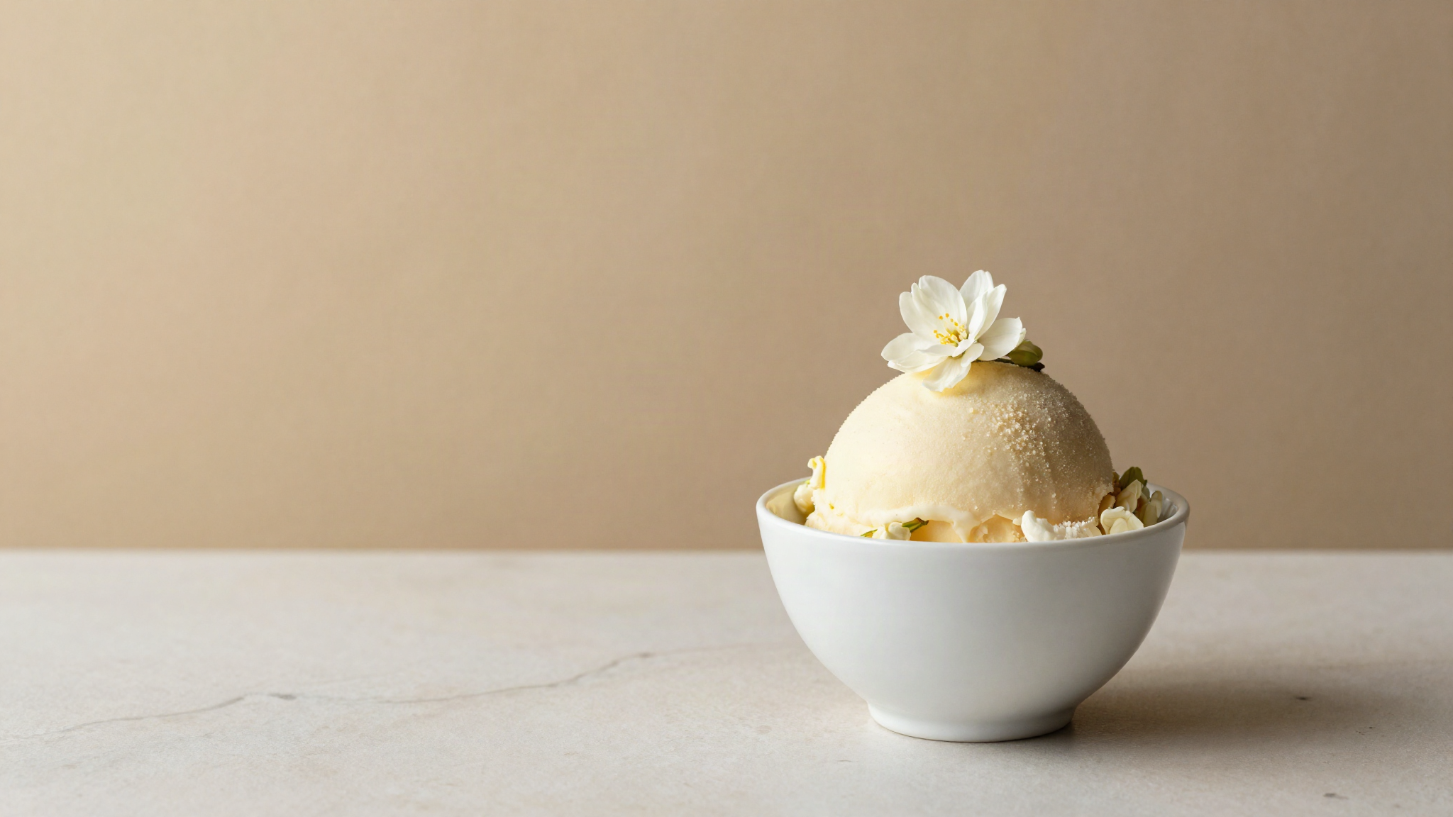 A finished serving of pale jasmine gelato in a refined white ceramic cup garnished with a single jasmine blossom