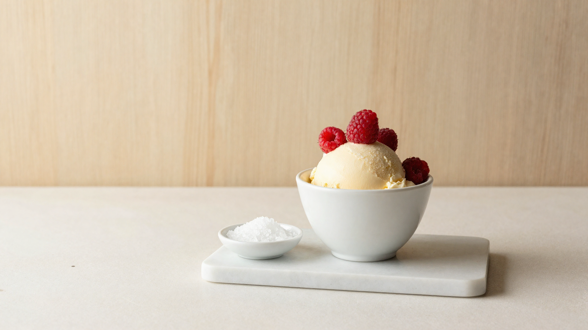Keto gelato in a white ceramic cup beside a dish of allulose crystals on marble