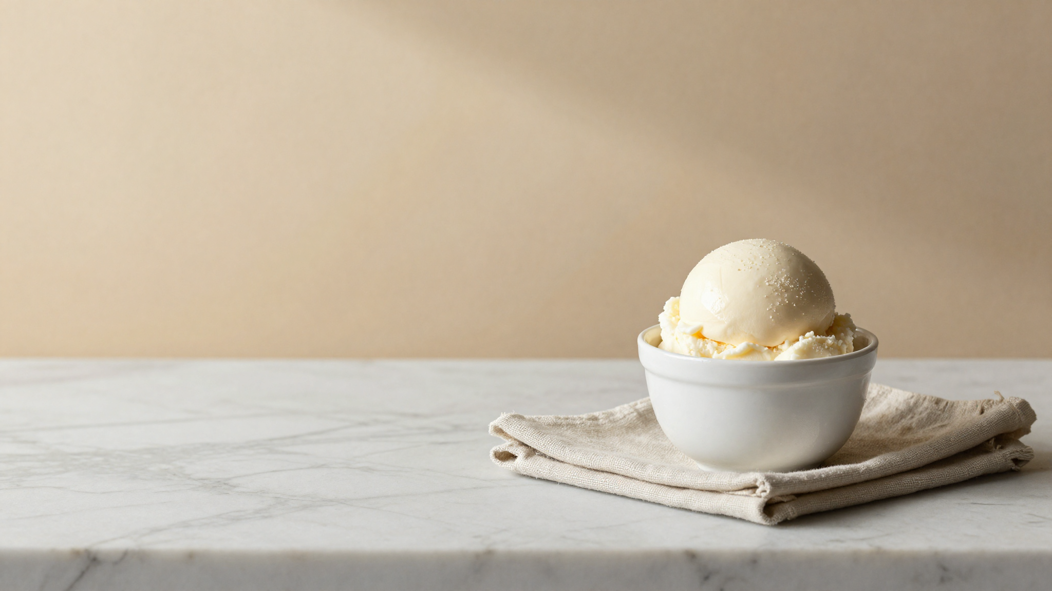 A smooth scoop of pale white milk gelato in a small white ceramic cup with a linen napkin