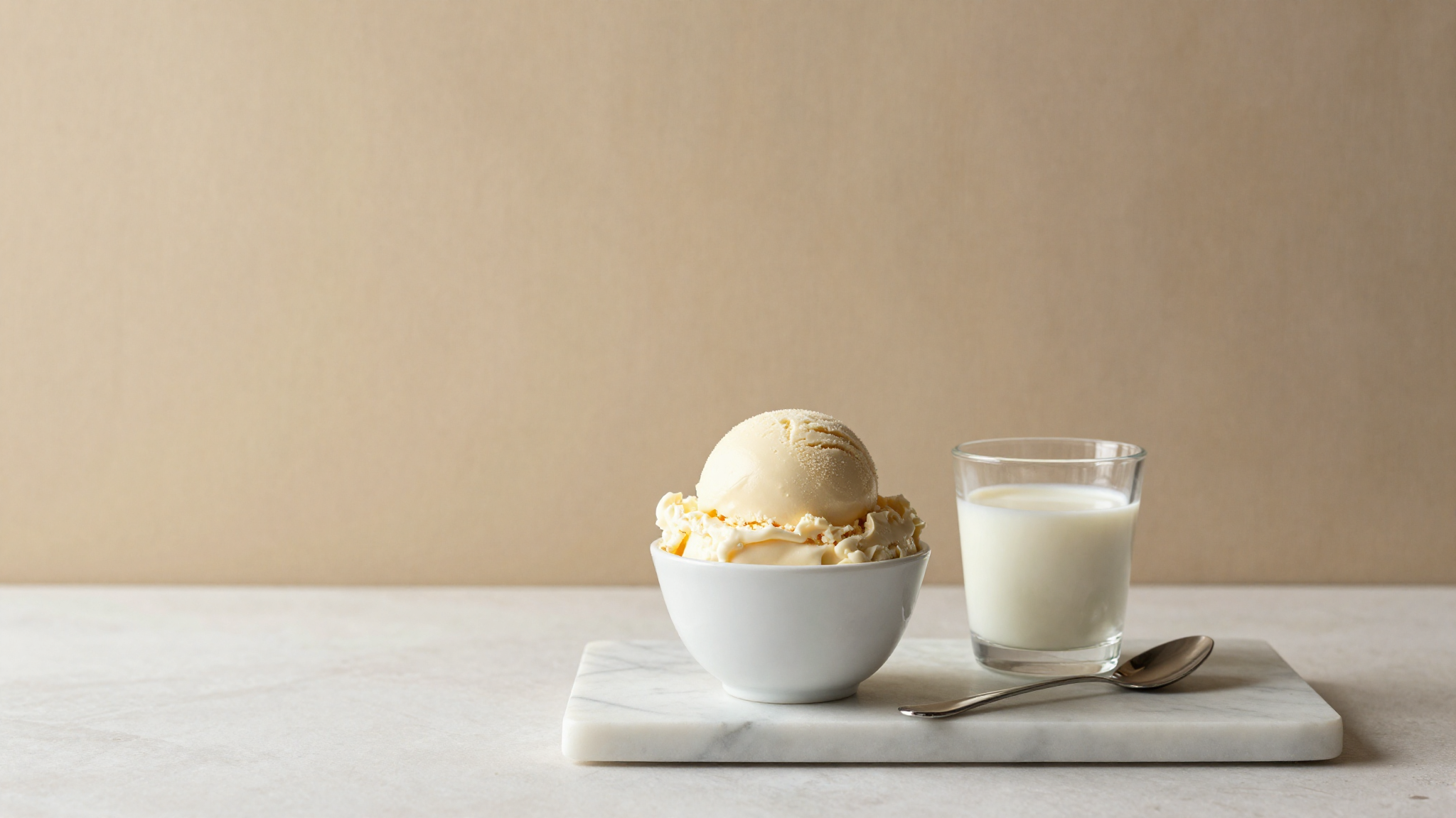 A finished scoop of creamy gelato in a ceramic cup beside a glass of milk on marble