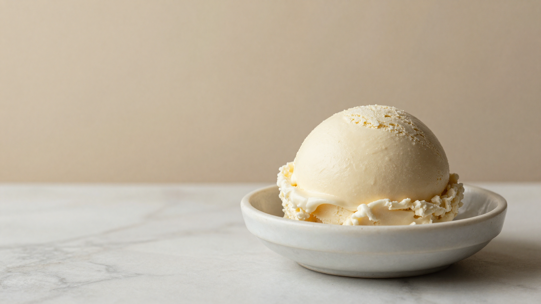 Smooth scoop of pale lactose-free gelato in a ceramic dish on marble