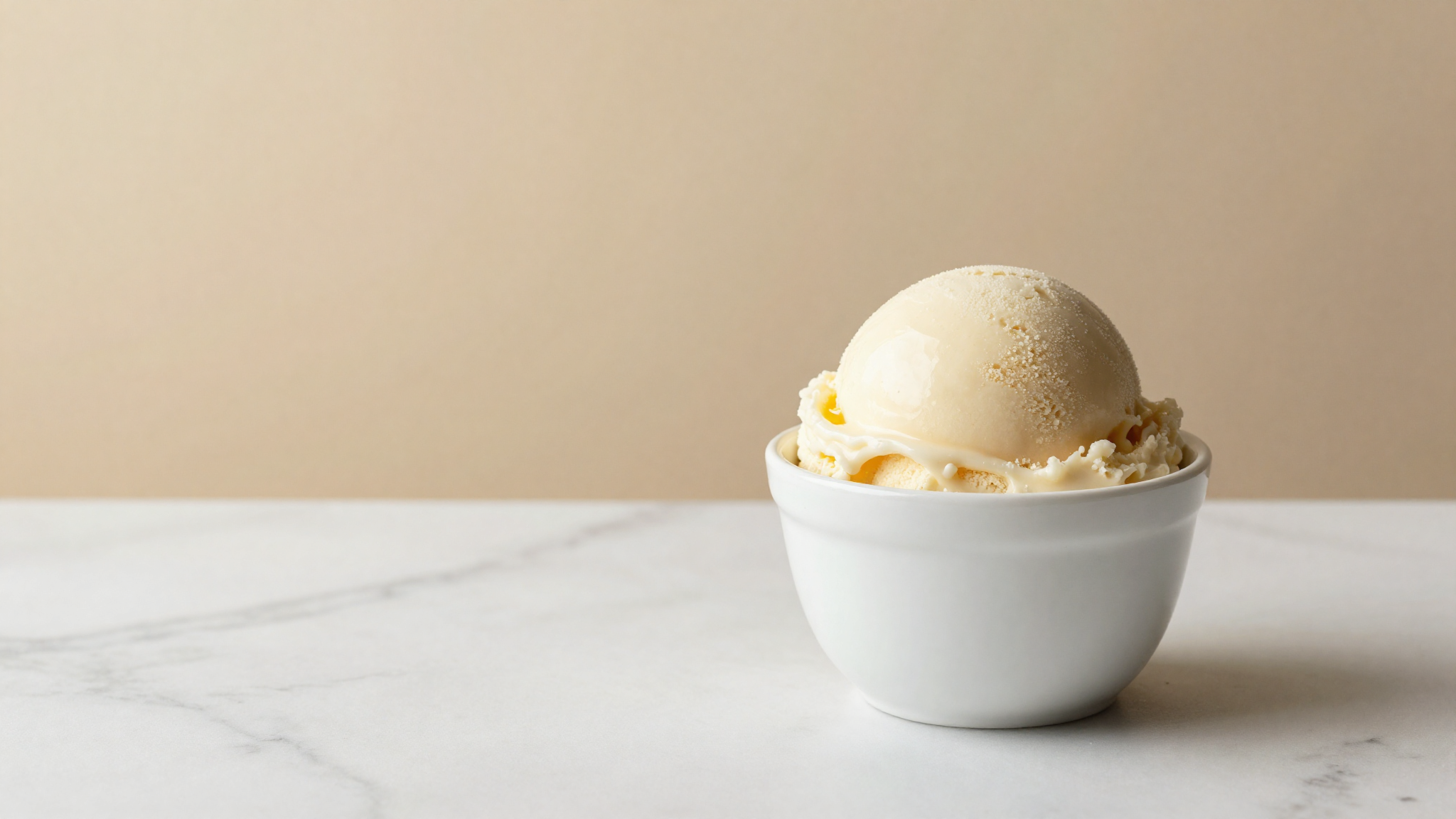 Single dense smooth scoop of pale gelato in a white ceramic cup on marble, glossy clean emulsified texture