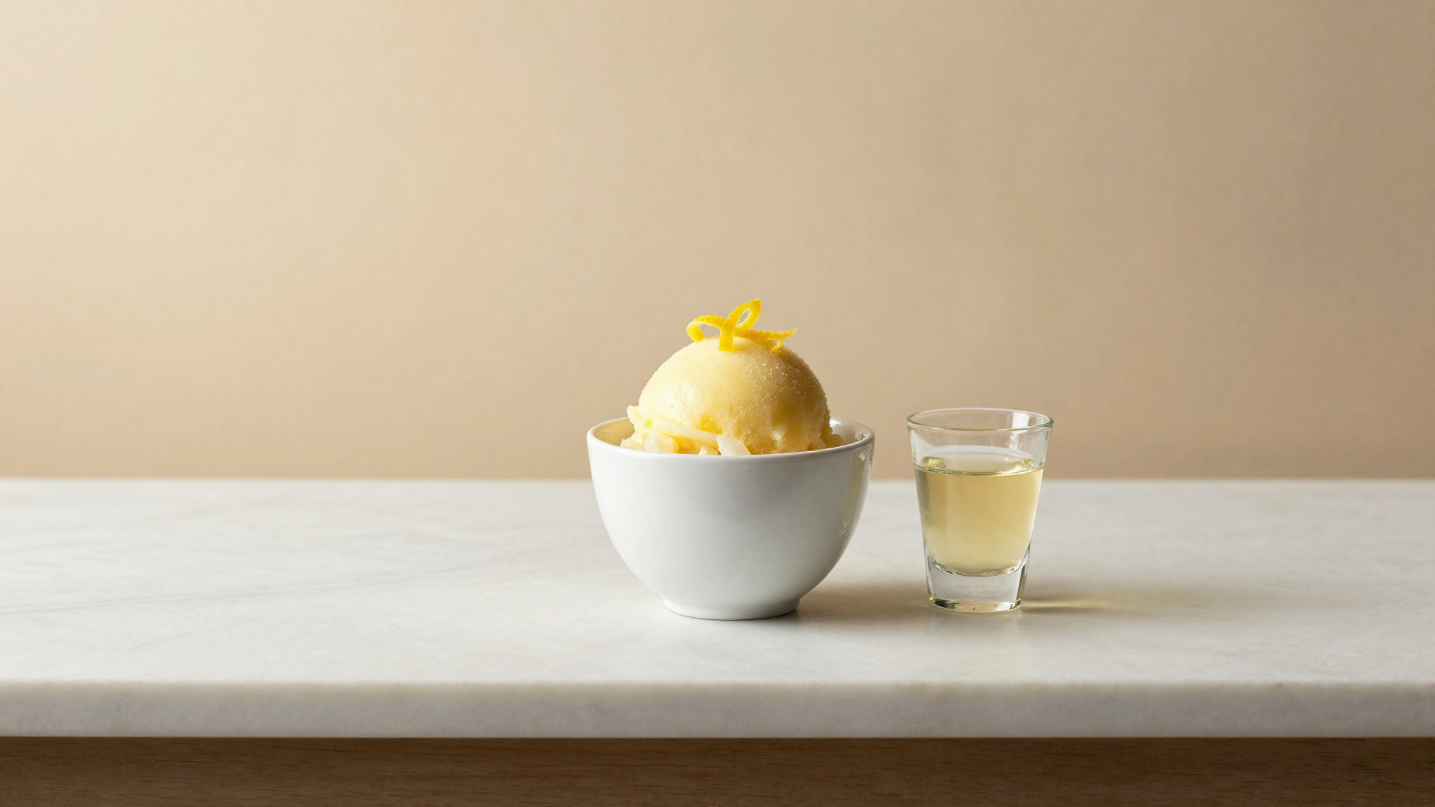 Limoncello sorbetto in a small white ceramic cup with lemon zest twist beside a glass of limoncello