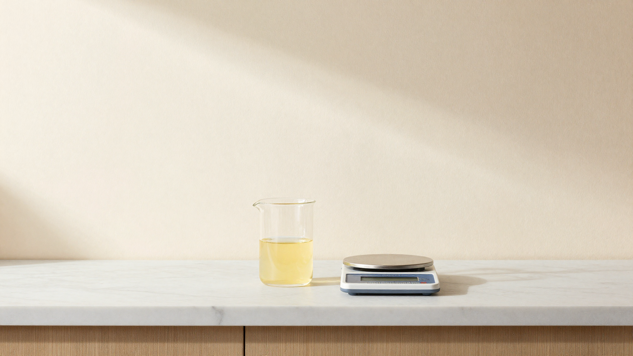 A glass beaker of pale yellow limoncello beside a digital precision scale on white marble