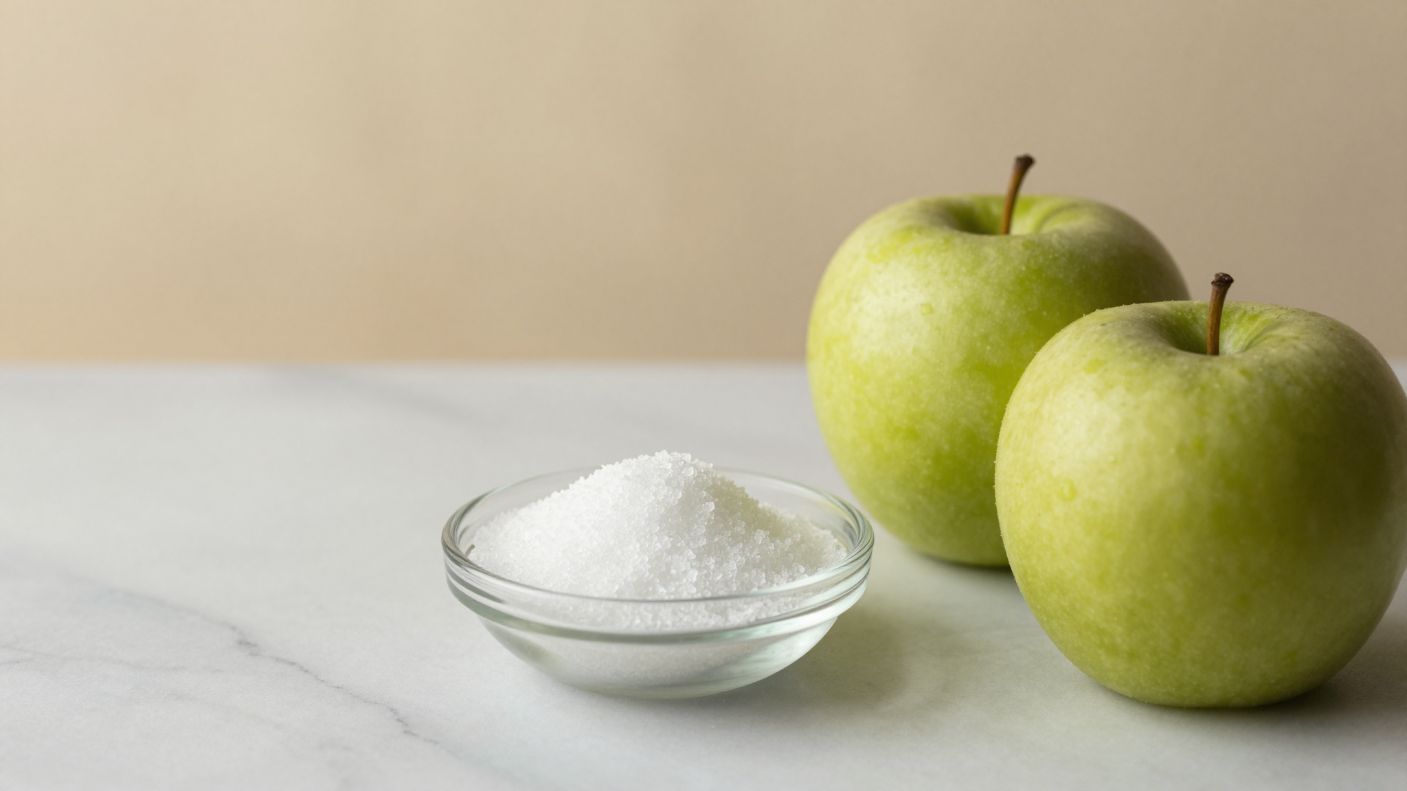 Fine white malic acid crystals in a glass dish beside two green apples on marble