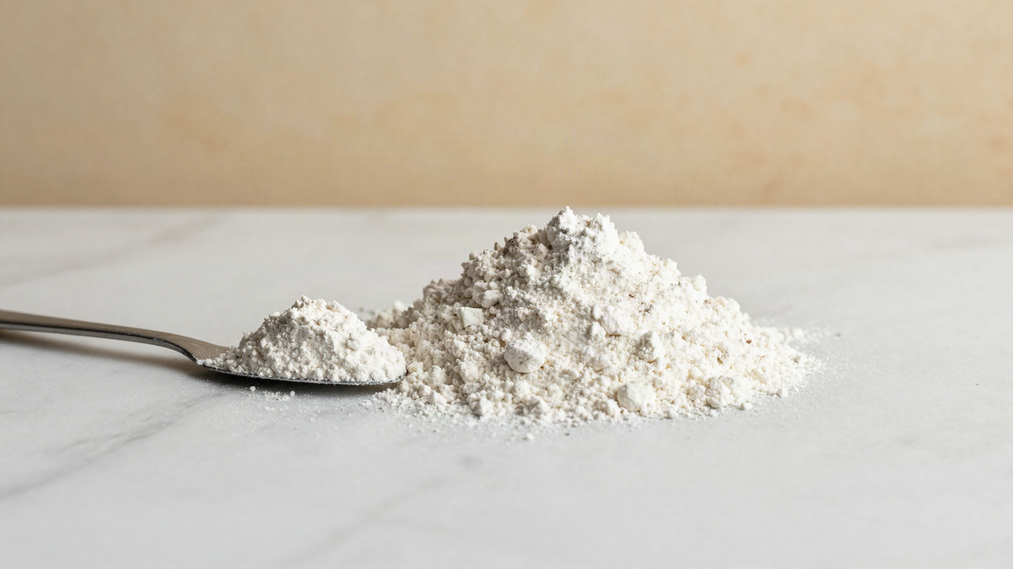 A soft mound of fine white maltodextrin powder beside a small steel spatula on marble