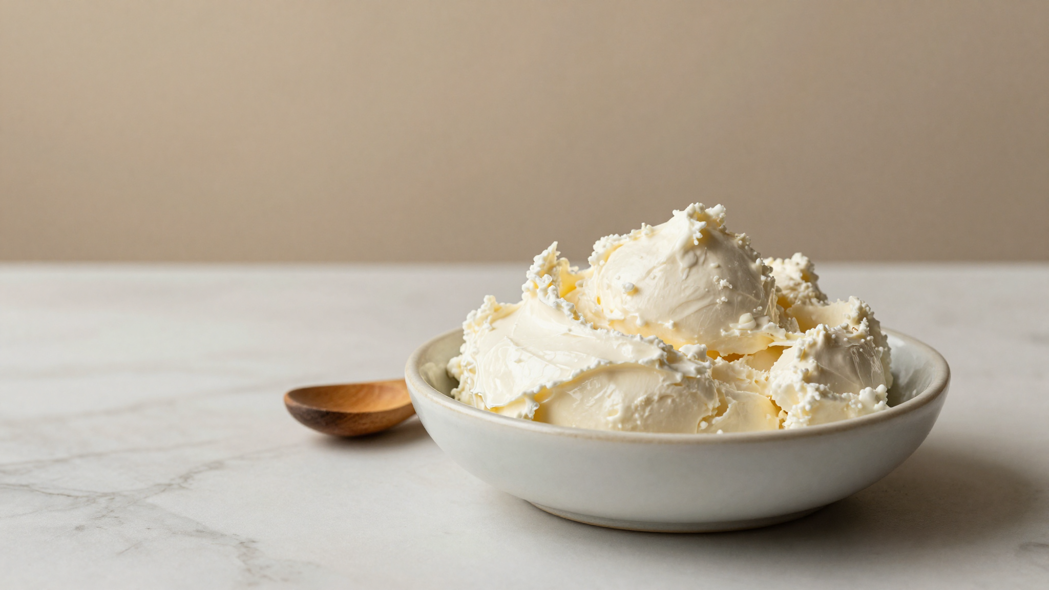 Fresh creamy mascarpone in a porcelain bowl on white marble in italian artisanal lab style