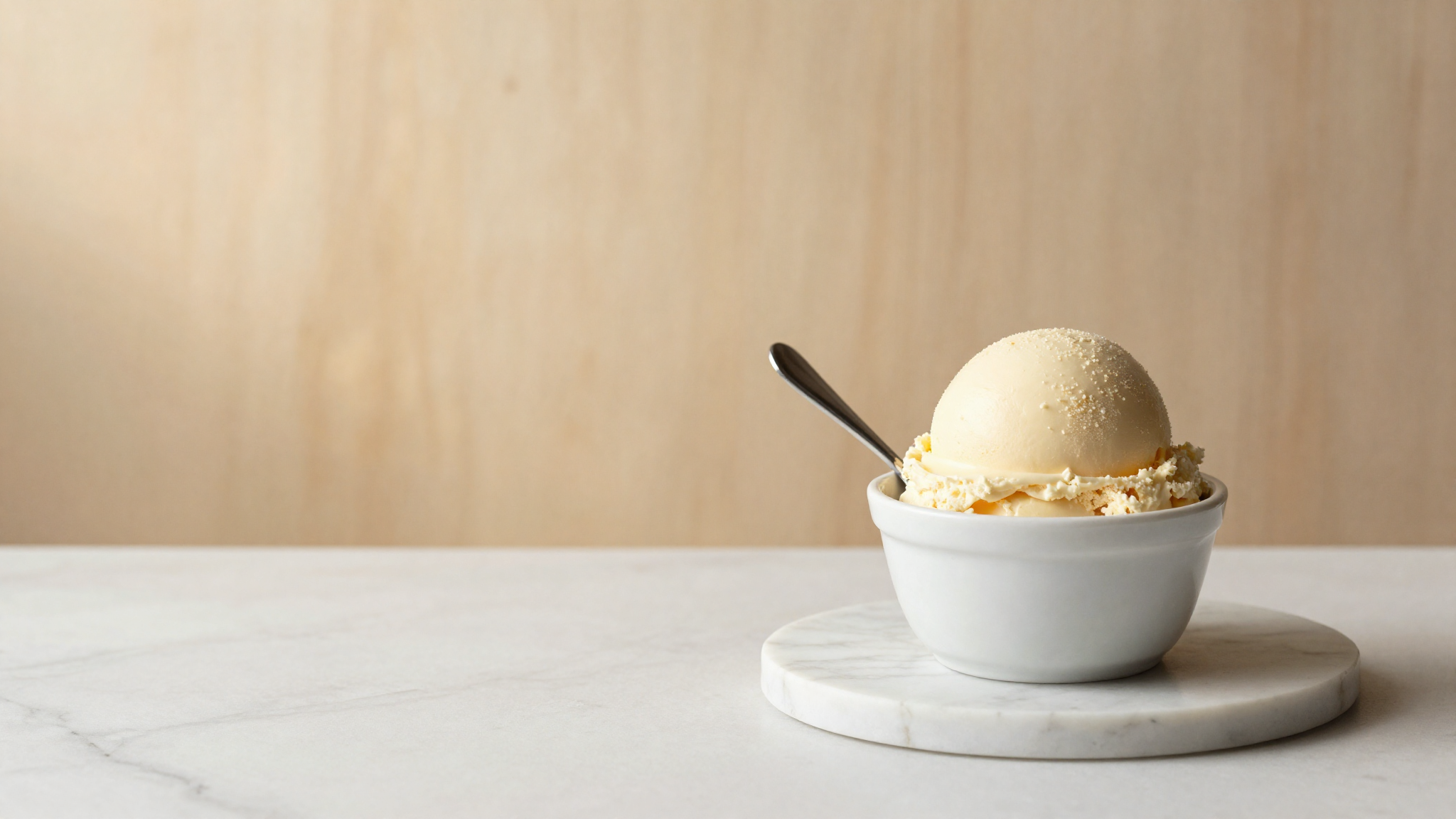A dense scoop of pale cheesecake gelato in a ceramic cup with a spoon