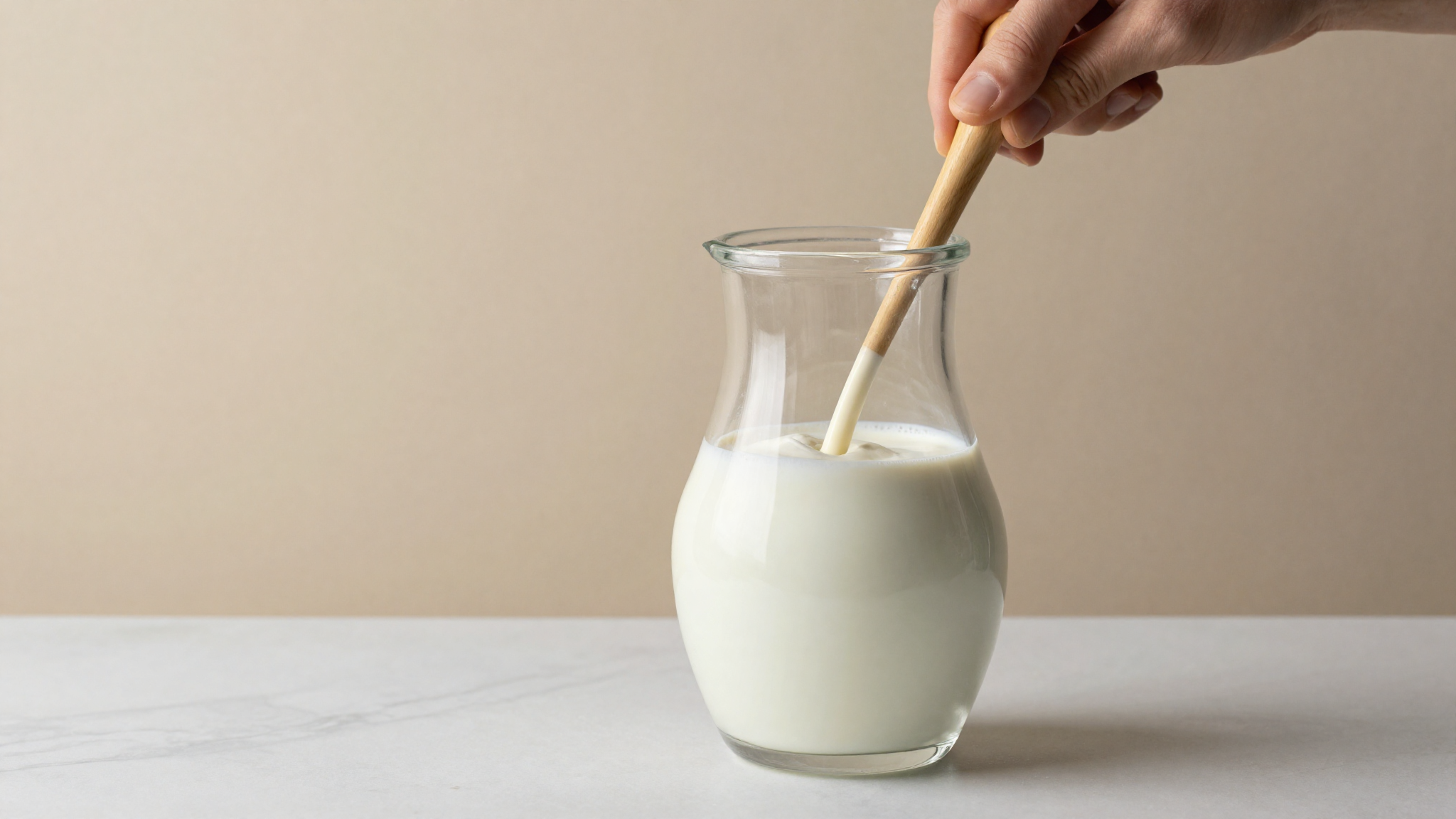 Pale milk protein concentrate powder being whisked into a jug of milk