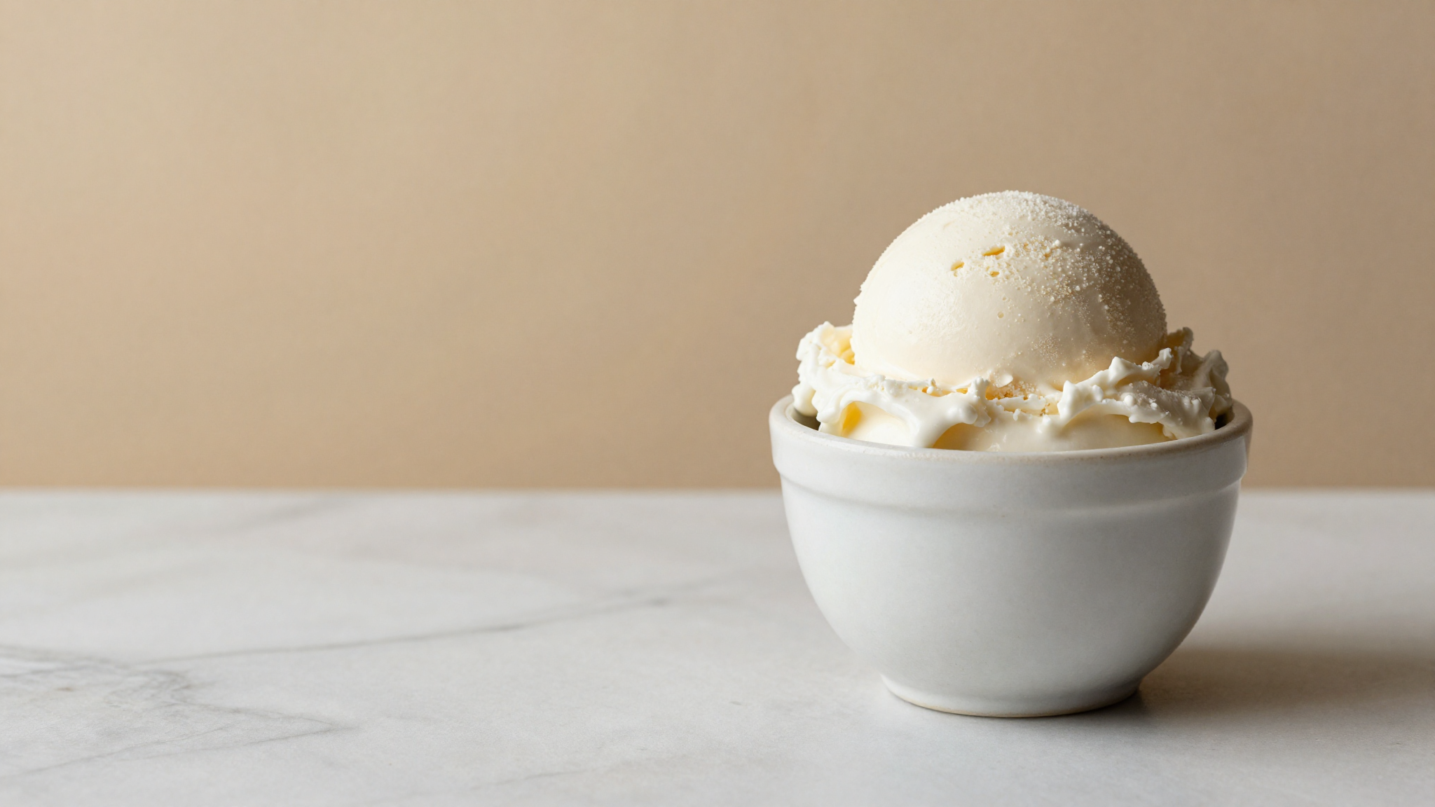 A single pale scoop of protein-rich gelato in a white ceramic cup on marble