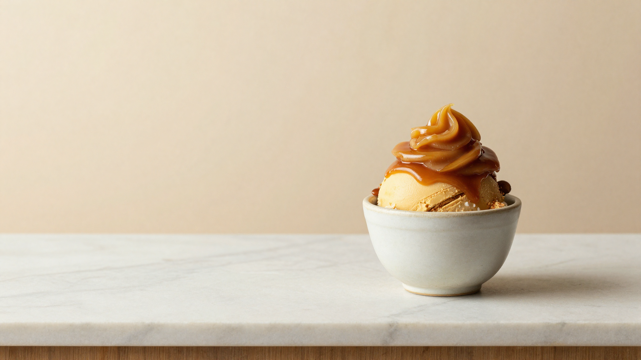 A finished serving of miso caramel gelato in a small ceramic cup with a glossy caramel swirl on top, on white marble