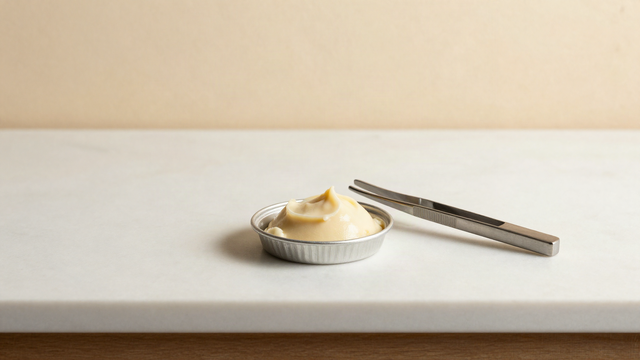 Small round aluminium sample pan holding a thin smear of pale gelato mix on a laboratory bench beside stainless tweezers