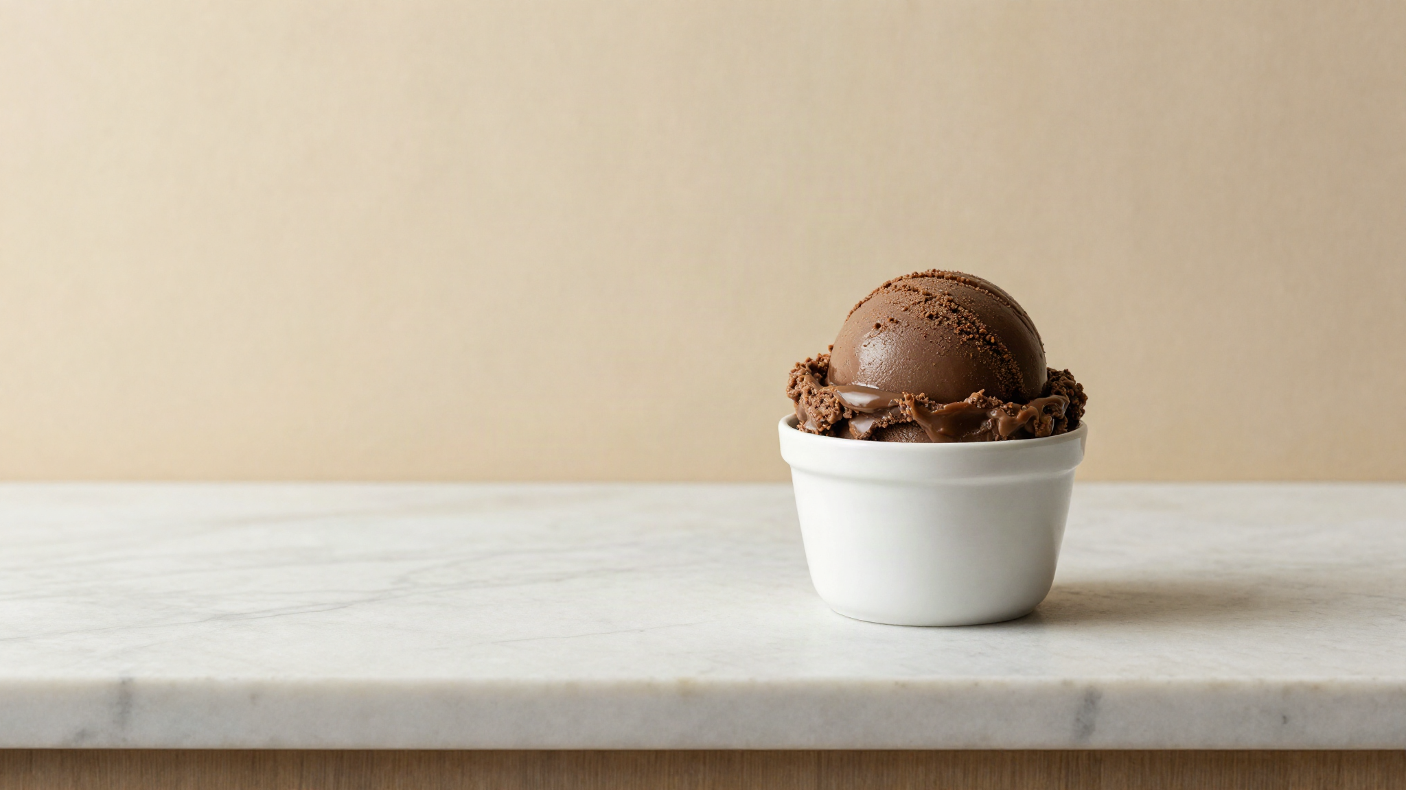 Two scoops of dark caramel coloured gelato in small white ceramic cups on a marble counter