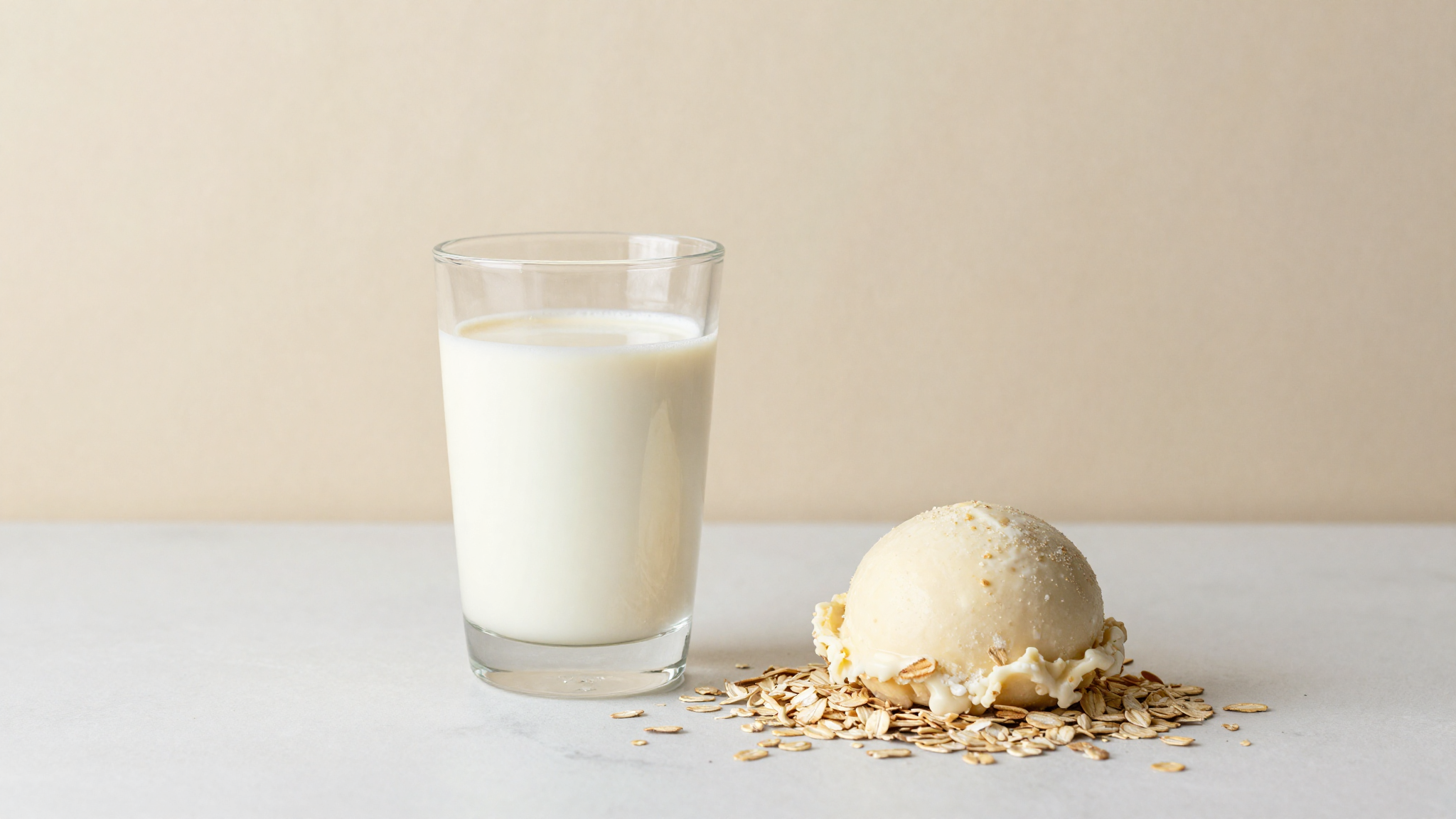 Scoop of vegan oat milk gelato in a ceramic cup beside oats on marble